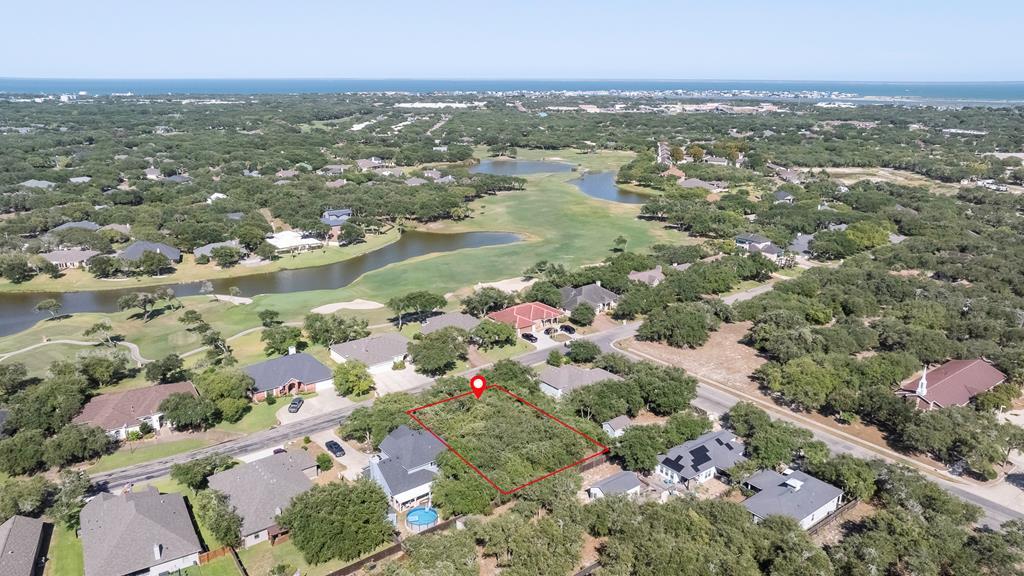 Aerial view of residential area in Fulton, Texas, highlighting available lot with red outline, surrounded by homes, greenery, and proximity to water features, emphasizing real estate opportunities in the region.