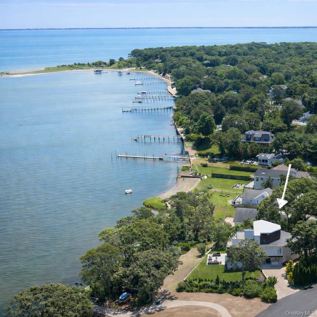 Set on a peaceful stretch of Shinnecock Bay in Hampton Bays, this sleek new-construction home sits atop one of the area's highest points, offering unobstructed water views from nearly every room. Floor-to-ceiling windows and an open layout create seamless indoor-outdoor living. Three floors, five bedrooms, and four and a half baths, including four en suites — one on the ground floor. Four of the five bedrooms open directly to a deck or garden, with wraparound decks on the second and third floors offering sweeping water views. First and second-floor laundry rooms add everyday convenience. Outside: a heated pool, private dock, and beach access to Shinnecock Bay for boating and kayaking, plus a fire pit and outdoor shower for classic coastal evenings.