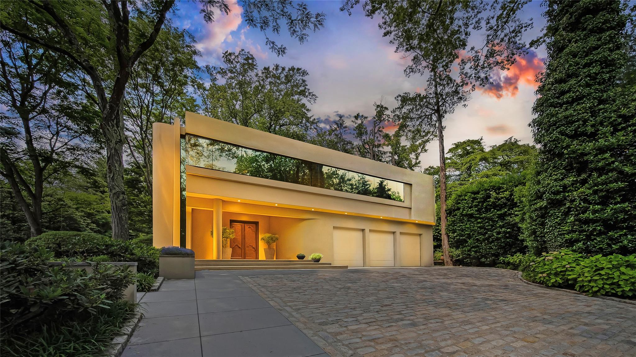 Welcome to a sanctuary in North Hills - a one-of-a-kind Frank Lloyd Wright–inspired contemporary masterpiece, creating a living space that feels both timeless and inviting. The home echoes Wright’s approach, using natural local material such as wood and stone, with strong horizontal lines and clean geometry. Wright also used windows and skylights to bring natural light deep into interiors and frame views of the landscape, and integrated art and custom designed elements throughout his homes, all elements incorporated throughout this home.

Thoughtfully conceived by renowned architect Tim Maldonado, this 1.30-acre, 7,200 +/- sqft estate in the village of North Hills offers a rare opportunity to experience refined luxury in a serene, private setting just minutes from New York City and the Hamptons. The 4 Bedroom, 7 bathroom residence was designed with complete privacy and artistic expression in mind. Clean lines, natural materials, and dramatic spatial relationships foster a fluid connection between indoors and out. Positioned along the primary street frontage and balanced by a sculptural cottage at the far end of the combined parcels, the estate becomes a secluded preserve—an immersive sanctuary that celebrates sculpture, serenity, and modern luxury. 

Upon entry, the entrance features an elegant pair of intricately carved wooden doors imported from Paris. A sleek, modern sculpture stands to one side, contrasting beautifully with the natural elements. The overall design harmonizes traditional and contemporary styles, making the entrance both charming and sophisticated. The home is further distinguished with expansive flamed Canadian granite floors, while a striking water feature frames the floating steel staircase. The chef’s kitchen is as functional as it is beautiful, featuring top-tier Miele, Subzero and Wolf appliances, bespoke European rift oak cabinetry, custom Ann Sacks tile, granite countertops, and a dedicated coffee station and pantry. 

Upstairs, the home continues to impress with a collection of serene, retreat-like bedrooms, two with its own en-suite bath, walls and ceilings finished in high-gloss lacquer for a refined, modern aesthetic. The primary suite is a private sanctuary, offering a spa-inspired bath with an oversized steam shower, multiple rain and body shower heads, a deep soaking tub, dual walk-in closets, a built-in coffee station, and a private balcony overlooking the grounds. 

Nestled within lush, manicured grounds, the property offers an outdoor oasis, complete with a striking in-ground heated pool and spa, framed by mature fig trees, vibrant hydrangeas, a Koi pond, and expansive lounging and dining areas—ideal for alfresco dining, entertaining and quiet relaxation. Adding to the estate’s unique appeal is a separate, award-winning cottage known as “Waterfall Pavillion” that received a Design Award of Merit from the Society of American Registered Architects (SARA) New York in the 2007 Design Awards. Designed with the warm, rustic charm of a mountain retreat, the pavilion features soaring ceilings with exposed beams, rich custom millwork, oversized windows with automated blinds, and refined finishes throughout creating a serene, Aspen-like atmosphere. The Pavillion includes a full kitchen outfitted with Wolf appliances, a luxurious spa-style bath, and a versatile flex space. 

No detail has been overlooked in the ongoing care and maintenance of the property. A heated three-car garage, finished lower level with kitchen, 1,000 bottle count temperature-controlled wine cellar, updated five-zone central AC, reflective tinted glass windows, 2 commercial grade generators, and a durable rubberized roof all speak to the same level of thoughtfulness and quality that defines every inch of this remarkable home. 

This property is more than a residence—it’s a work of art. A private sanctuary where contemporary design, nature, and luxury converge in one of Manhasset’s most prestigious communities.