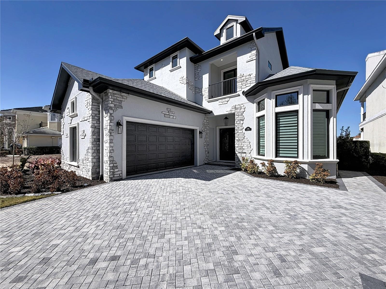 One or more photo(s) has been virtually staged. Located at 7394 Gathering Court within the exclusive gates of Reunion Resort, this brand-new contemporary estate captures sweeping views of the renowned Watson Golf Course and delivers an elevated standard of resort-style living. A grand circular paver driveway and custom iron double doors set the tone, opening to a gallery-style foyer illuminated by tiered gold-and-crystal chandeliers and complemented by wood-look porcelain tile throughout. The dramatic great room showcases soaring 16-foot vaulted ceilings with coffered detailing and expansive impact-resistant windows that frame the lush fairways like artwork. Designed for both beauty and performance, the chef’s kitchen features solid wood custom cabinetry, a bold navy statement island topped with 3-inch mitered quartz, professional-grade appliances including a gas range, and a hidden walk-in pantry that preserves a clean, modern aesthetic. The main-level primary suite offers a private retreat with tray ceilings, custom walk-in closets, and a spa-inspired zero-entry shower with frameless glass and designer finishes. A rare highlight is the fully self-contained private-entry apartment complete with its own balcony, walk-in shower, and dedicated laundry, ideal for guests, multigenerational living, a private office, or added flexibility. Expansive accordion doors create seamless indoor-outdoor flow to the extended paver patio and custom summer kitchen, perfectly positioned to enjoy tranquil golf course views. Additional features include an epoxy-finished garage, oversized laundry room with custom cabinetry and sink with access to world-class amenities including multiple resort pools, fitness facilities, 24-hour guard-gated security, with HOA-covered internet, cable, and lawn care for effortless living. This exceptional residence blends architectural artistry with the ease and elegance of everyday luxury.