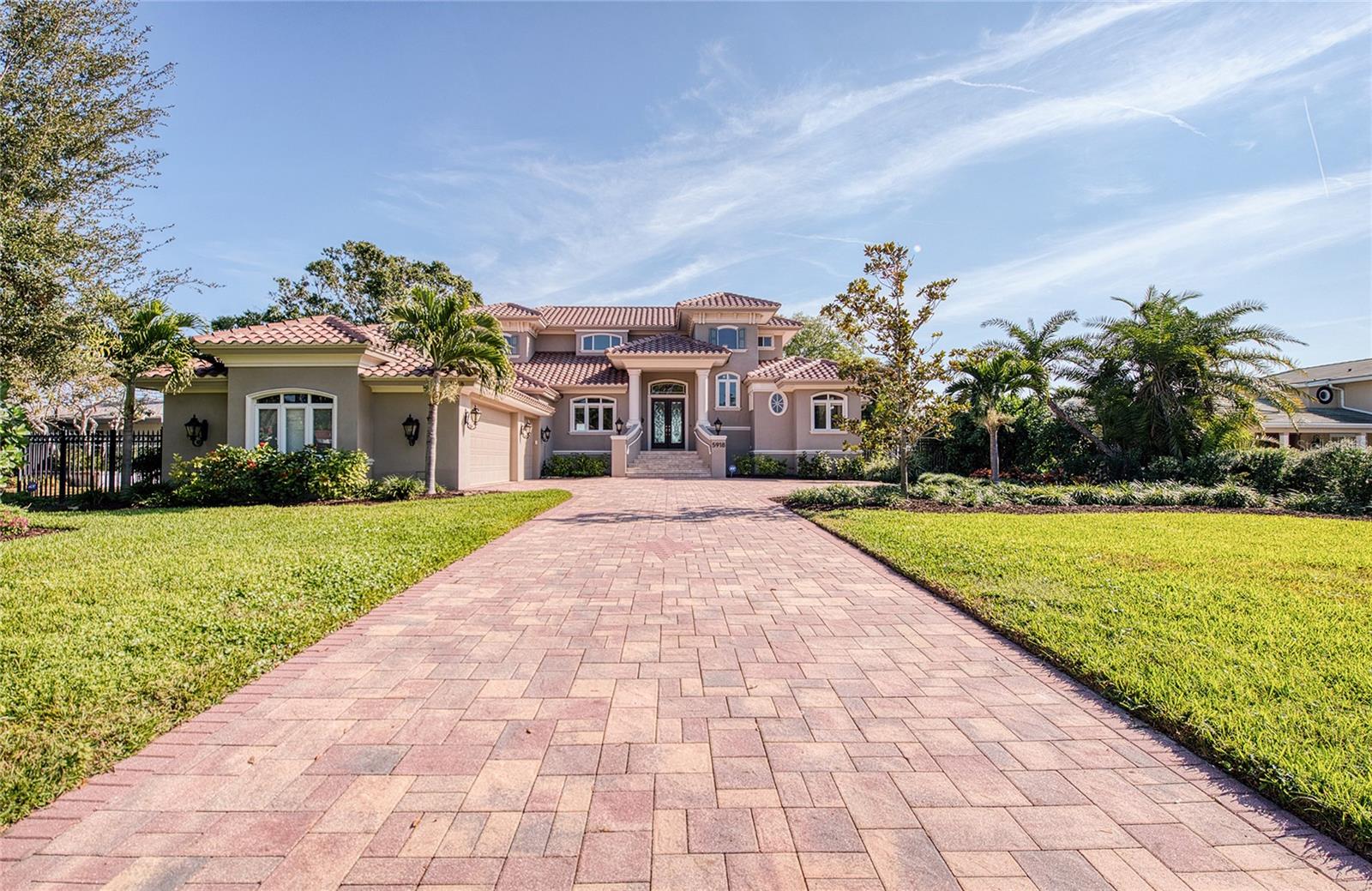 Located in the desirable Bahama Shores neighborhood, this exceptional Mediterranean-style waterfront home offers a rare blend of refined design and relaxed coastal living. Approached by a picturesque, tree-lined boulevard off 60th Avenue South, the property immediately impresses with its custom brick driveway and commanding presence along the shores of Tampa Bay. Inside, the home features 10-foot ceilings throughout, complemented by crown molding and architectural ceiling details that create an open yet sophisticated atmosphere. The thoughtfully designed kitchen is equipped with custom cabinetry, dual convection ovens, a spacious walk-in pantry, and a butler’s pantry with a dedicated wine refrigerator. The kitchen flows naturally into the main living area, where expansive windows frame stunning bay views. The primary suite is located on the main level and serves as a private sanctuary, featuring a fireplace and an oversized bathroom designed with spa-like comfort in mind. An adjoining bonus room or office provides flexible living space, while a second en-suite bedroom on the first floor offers added convenience for guests or multi-generational living. Outdoor living is a standout feature, with wraparound decks spanning the back of the home—ideal for entertaining, dining outdoors, or simply enjoying sunsets, boat traffic, and marine wildlife. The upper level includes three additional bedrooms and two full bathrooms, along with balcony access that further showcases the surrounding water views. Additional amenities include an oversized three-car garage with ample room for recreational equipment, a downstairs laundry area with an extra refrigerator, and a seawall completed in 2014. Notably, the home has never experienced hurricane-related flooding, and a new roof was installed in 2025, offering added peace of mind. The property sits on an impressive 94 x 220 waterfront lot, providing both privacy and breathtaking scenery. This is a rare opportunity to own a beautifully maintained waterfront residence in one of the area’s most sought-after neighborhoods.