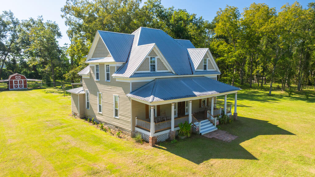 If you have been searching for a true South Georgia farmhouse with historic character, room to spread out, and the infrastructure for country living, this 5-bedroom, 3-bath home on 9.41 acres deserves a closer look! Built in 1900 and offering approximately 2,814 square feet, this classic two-story farmhouse is set among mature hardwoods, towering shade trees, and beautiful surrounding farmland. The exterior immediately stands out with its metal roof, multiple front gables, decorative shingle accents, traditional columns, and an expansive covered front porch made for rocking chairs and slow mornings. Inside, the home is filled with details that showcase its history and personality. A wide central hallway and traditional staircase welcome you inside, while tall windows throughout bring in abundant natural light. Multiple rooms feature fireplaces with brick or stone surrounds and traditional mantels, and you'll find a mix of wood-look flooring, extensive trim work, beadboard, wood accents, and impressive original-style wood plank walls upstairs. The spacious living areas provide plenty of flexibility for everyday living and entertaining, while the formal dining room makes a statement with its warm wood accent wall, fireplace, and chandelier. The generously sized kitchen offers an abundance of white cabinetry and countertop space, a double-basin sink positioned beneath a window, open shelving, and an adjoining walk-in pantry with extensive shelving. Additional interior highlights include French doors, a sliding barn-style door, ceiling fans, generously sized bedrooms, and bathrooms full of farmhouse character, including a clawfoot tub, antique-style vanity, separate shower, and convenient laundry area. Upstairs is especially unique, with a large landing and oversized rooms wrapped in rich natural wood plank walls, traditional wood doors and trim, plentiful windows, and an additional bath. Outside, the 9.41-acre property continues to impress with large open lawn areas, mature trees draped with Spanish moss, wooded sections, fencing, multiple gated areas, and a distinctive gated entrance. Numerous outbuildings provide exceptional versatility, including a large metal workshop with a roll-up door, concrete floor, extensive overhead lighting, equipment space, and attached covered lean-to; a rustic barn with fenced animal areas; a red barn with horse stable stalls and covered extensions on both sides; additional storage buildings; and another detached building featuring a simple kitchen setup. There is also a covered brick patio area beside the home for outdoor gatherings. Whether your plans include a hobby farm, horses or livestock, gardening, equipment storage, woodworking, homesteading, or simply enjoying the privacy and slower pace of country life, this property offers space and possibilities that are increasingly hard to find. Come experience the history, character, and country lifestyle this one-of-a-kind 1900 farmhouse on 9.41 acres has to offer!