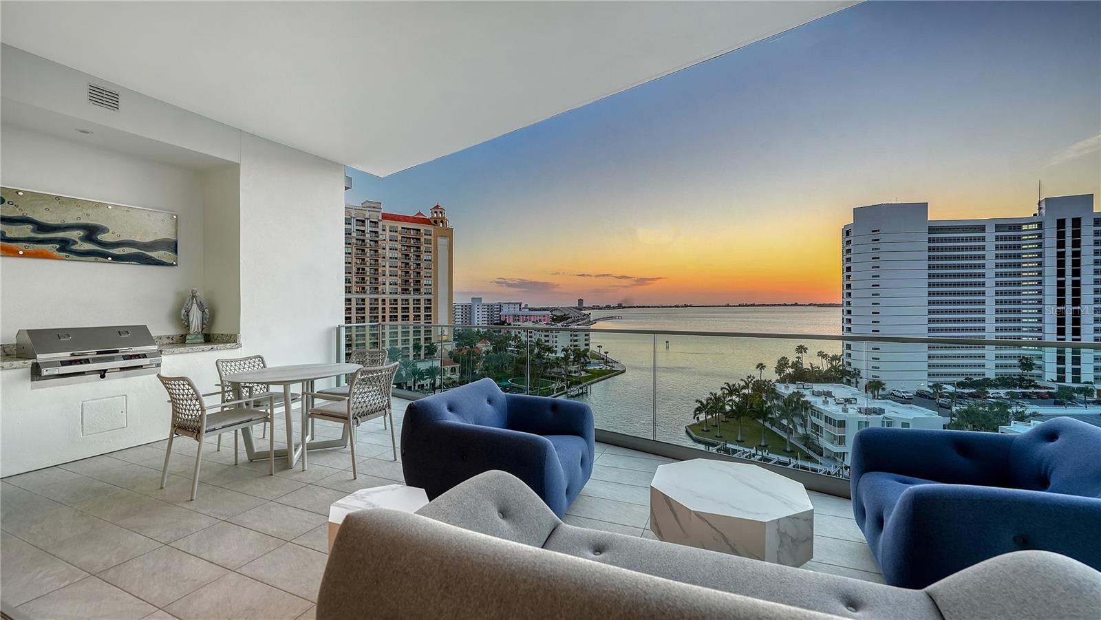 One-of-a-kind and completely custom, Residence #805 at The Ritz-Carlton Residences in downtown Sarasota is a rare offering in a premier waterfront location. Perched on the eighth floor, this highly customized corner residence is uniquely positioned with direct bridge access to The Ritz-Carlton Hotel—placing world-class amenities, valet services, and fine dining at Rufa, Jack Dusty, and Ocean Prime just seconds from your private entry. Offered furnished and professionally designed, this exceptional corner residence showcases panoramic views of Sarasota Bay, the John Ringling Bridge, the city skyline, and vistas that stretch toward the Gulf of Mexico. With more than 3,600 square feet of interior living space, this three-bedroom plus den condominium delivers refined waterfront living within a Ritz-Carlton managed property. A private residents-only elevator opens directly into the foyer, where illuminated built-in art displays and natural wood accents create a gallery-style arrival. The great-room layout is framed by 11-foot ceilings throughout and walls of floor-to-ceiling glass, maximizing water and skyline views from nearly every vantage point. Porcelain tile flooring extends throughout, reinforcing the seamless flow of the open design. The living area is anchored by a dramatic water vapor fireplace and a custom-designed bar with dual beverage refrigerators and an art-inspired wine storage wall. Expansive sliders open to the main terrace, where a summer kitchen and glass railings preserve uninterrupted bay views. The chef’s kitchen blends architectural precision with performance, appointed with Wolf professional-grade appliances concealed behind sleek cabinetry, a five-burner gas cooktop with pot filler, dual built-in ovens with warming drawer, custom quartzite countertops, tile backsplash, and an oversized waterfall-edge island with dine-in seating. A walk-in pantry enhances functionality and organization. The northwest-facing primary suite serves as a private sanctuary, complete with its own bayfront terrace, custom inset lighting, built-in workstation, floating shelves, and a dry bar with beverage refrigerator. Dual walk-in closets feature motion lighting and glass display cabinetry. The spa-inspired bath includes dual vanities, a central island with bench seating, a stone shower with multiple showerheads and built-in bench, and a private water closet. Two guest suites are arranged in a split layout for added privacy, each with en-suite baths and custom built-ins. The den, framed by floor-to-ceiling glass and integrated shelving, functions beautifully as a home office or media lounge. Additional features include Crestron smart home system controlling the lighting, shades, audio, and video; Nest thermostat; three private terraces with glass railings; one of only ten oversized private one-car garages, featuring built-in storage and two full-size wine coolers accommodating 166 bottles each; and an additional oversized parking space directly across from the private garage. As part of a Ritz-Carlton managed property, residents enjoy an unmatched level of service and amenities, including a 70-foot heated lap pool, resort-style pool and spa with cabanas, poolside bar, club and social rooms, news and sports cafe, fitness center with yoga studio, boardroom, multi-purpose room, dog park with pet washing station, 24-hour concierge, valet service, and on-site management. In-residence dining, housekeeping, and laundry services are also available.