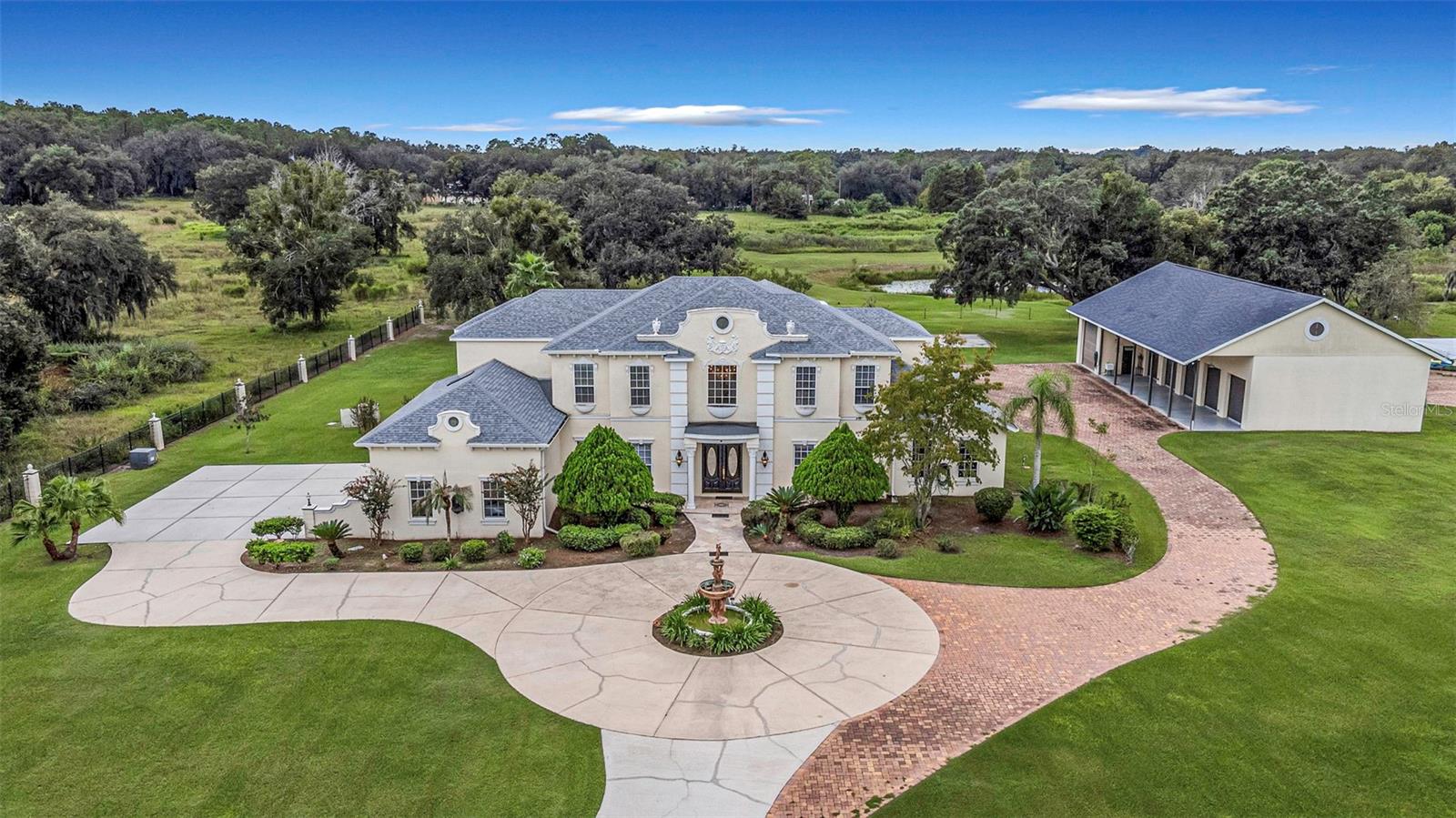 One-of-a-Kind Luxury Estate on 10 Acres in Wesley Chapel!  This custom-designed masterpiece gives you a rare opportunity to own a unique compound.  The main residence offers 5,461 square feet of luxurious living space, plus a separate 805 sq feet Guest House, a gorgeous Saltwater Pool & Spa and a total of 9-Car Garage.  From the moment you arrive, you're welcomed by the double, gated entry, followed by the picturesque driveway, water fountain & circle drive.  Elegant decor & amazing details awaits you as you step inside the grand foyer, highlighted by gleaming marble floors, a stunning curved staircase, soaring high ceilings and spectacular chandelier.  Featuring 4 spacious bedrooms, 4 full bathrooms, 2 half baths, private office, formal living room, grand dining room with French doors, high ceilings all the way to the 2nd floor and a Romeo & Juliet balcony above.  The luxurious master bedroom is on the first floor, has direct access to the screened lanai/pool area and has a beautifully appointed bathroom featuring dual vanities, granite countertops, a spa soaking tub, a dual head-walk through shower, French Travertine tile, and two walk-in closets. Upstairs has a 2nd master bedroom as well with an ensuite bathroom and walk-in closet.  There's also a state-of-the-art home theatre with lots of comfortable lounge chairs for movie night and popcorn.  At the heart of the home, the chef's kitchen is designed for both everyday living and entertaining. With 42-inch, wood cabinetry, granite countertops, double wall ovens, brand new refrigerator, an expansive center island, breakfast bar and a charming dining nook make this a space you'll love gathering in. The kitchen opens to the adjoining family room, complete with a fireplace, crown molding, and French doors that lead to your own private oasis.  Imagine spending sunny Florida afternoons lounging beside your saltwater pool, unwinding in the spa, or hosting friends and family on the covered, screened lanai. With a wet-bar area and pool bath, this outdoor living space is ideal.  Beyond the pool area is the private guest house, making it the perfect guest quarters, In-law suite, home gym/game room or mancave.  And for the car enthusiast or anyone wanting exceptional storage & workspace for hobbies, the 6-car, detached garage is a remarkable bonus!  The detached garage has 2,260 square feet, 6-car plus capacity, top-of-the-line car lift, extremely high ceilings, electricity and an air conditioned, oversized RV bay that can also serve as a workshop. The main home has a 3-car garage attached, giving you a 9-car garage in total.  In the backyard there's even more to enjoy, with a basketball court and fishing pond and plenty of land for a garden, room for horses and even a barn.  You are welcome to bring your boat, recreation vehicles, tractors, animals or whatever your heart desires, there's room for it all.  There are NO HOA fees, no CDD fees, and NO deed restrictions, giving you the freedom to enjoy your property and truly make it your own!  Conveniently located to I-75, with easy access to local dining, Publix grocery, Tropical Lagoons, Wiregrass Shoppes and top-rated schools.  This luxury property gives you the perfect blend of peaceful, country living with all the everyday conveniences. If you've been dreaming of a private estate with lots of land, this one-of-a-kind property is a must-see, give me a call for your private showing today!  A few photos have been virtually staged with furniture.