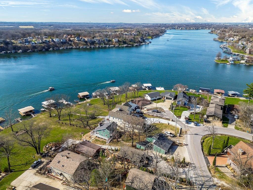 Looking for a main-channel home with sweeping water views, a spacious gently sloping lot, and exceptional docking space? This rare opportunity on the coveted extra-long lots of V block offers panoramic lake views from nearly every angle. The main level welcomes you with an open-concept layout designed for entertaining. The kitchen flows seamlessly into the dining and living areas, where an electric fireplace adds warmth and ambiance. The windows and sliding doors fill the space with natural light and showcasing breathtaking sunsets. Step outside to the wraparound deck — the perfect place to relax, host friends and family, or simply watch the activity on the water. A main-level bedroom, full bath, and laundry room provide convenience and flexibility for guests or everyday living. Upstairs, a loft overlooks the main living area, creating additional space for a home office or reading nook. The private primary suite offers a peaceful retreat, a full bath with double vanity, generous walk-in closet, and martini deck. The lower level expands your living and entertaining options even further. It features a third non-conforming bedroom and a half bath with the potential to convert to a full bath. The lower-level living area includes plumbing for a future wet bar and an electric fireplace, making it an ideal spot to unwind after a long day on the water. Walk out to the patio with a hot tub overlooking the expansive lakefront yard — perfect for bonfires, lawn games, and making memories that last all summer long. At the water’s edge, a covered, double-well dock with one PWC and two boat lifts, plus an additional swim dock provide ample space for docking and relaxing. Whether you enjoy early morning fishing or sunset cruises, this setup is ready for it all. Parking and storage are exceptional, a rare find on the lake. The property includes a three-car garage, with a workshop, additional parking for up to four vehicles, and a shared, paved drive to the edge of the lot.