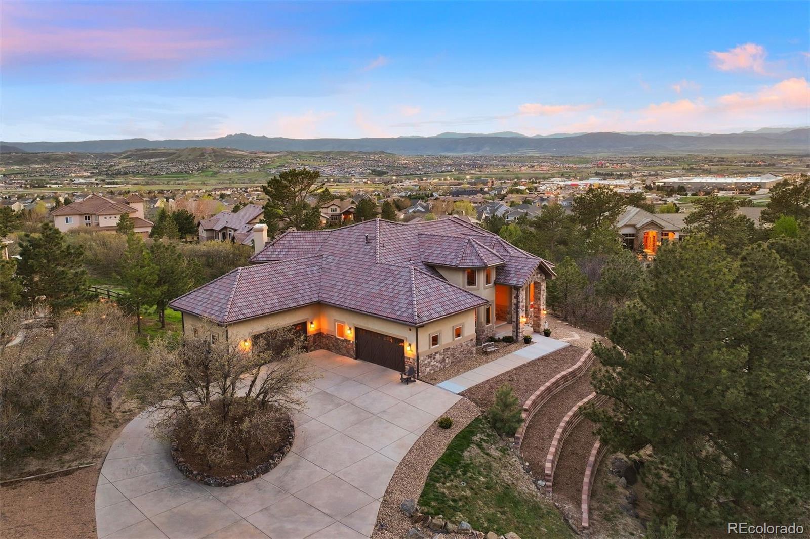 With panoramic Front Range views, Pikes Peak and “The Rock” in full sight, and a private position within Piñon Soleil, this home feels open to the horizon, yet sheltered in its setting. Every space is oriented to the surrounding landscape, creating a natural rhythm between indoors and out. With convenient access to Castle Rock, Parker, and Denver, dining, shopping, and daily essentials are always within easy reach.Curved walls, soaring ceilings, and rich layers of timber, stone, and brick create a sense of warmth and character. Double-arched front doors open to a sunlit foyer and great room, where a two-sided fireplace and walls of glass frame the mountain views. Cherry floors carry you through the main level and into a chef’s kitchen featuring high-end appliances, a generous island, a walk-in pantry, and a brick fireplace that naturally draws people in. Surrounded by windows, the eat-in area feels relaxed for daily living, while the formal dining room offers an elegant setting for hosting.This home offers the flexibility of two spaces that could serve as a primary suite, depending on how you live. The upper level provides a serene retreat with a private balcony, dual walk-in closets, a fireplace, and a spa-like bath. A clawfoot tub rests within a turreted bay window, perfectly positioned to take in the views. On the main level, a guest suite with its own five-piece bath and mountain outlook offers an equally comfortable option for main-floor living or long-term guests.The walk-out lower level is designed for entertaining and everyday enjoyment, with a spacious recreation room, wet bar, theater, and dedicated gym space. Outside, the flat backyard opens up new possibilities, from a future pool or garden to simply enjoying the space as-is. A four-car garage, circular drive, and additional parking add convenience. This is Colorado living at its most refined, elevated, private, and designed for a life well lived.