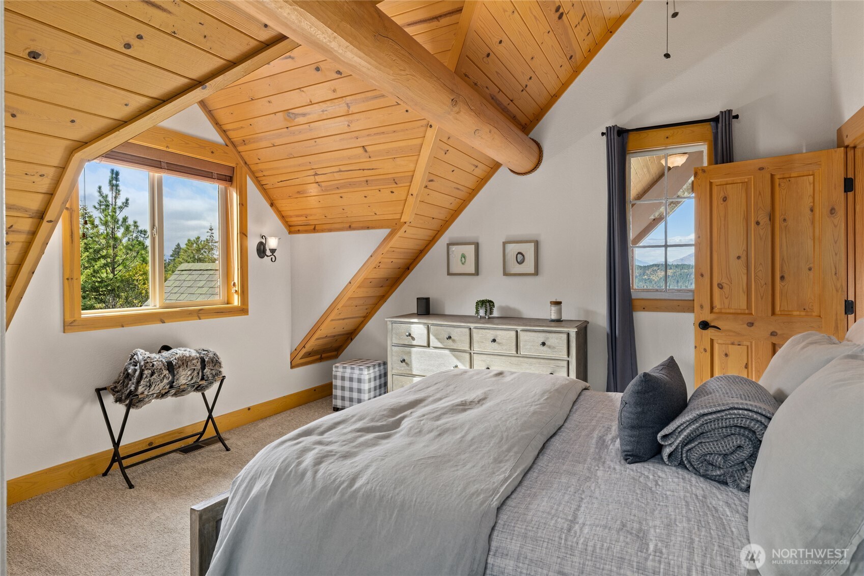 Guest bedroom with vaulted wood ceiling, exposed beams, abundant natural light, and mountain views.