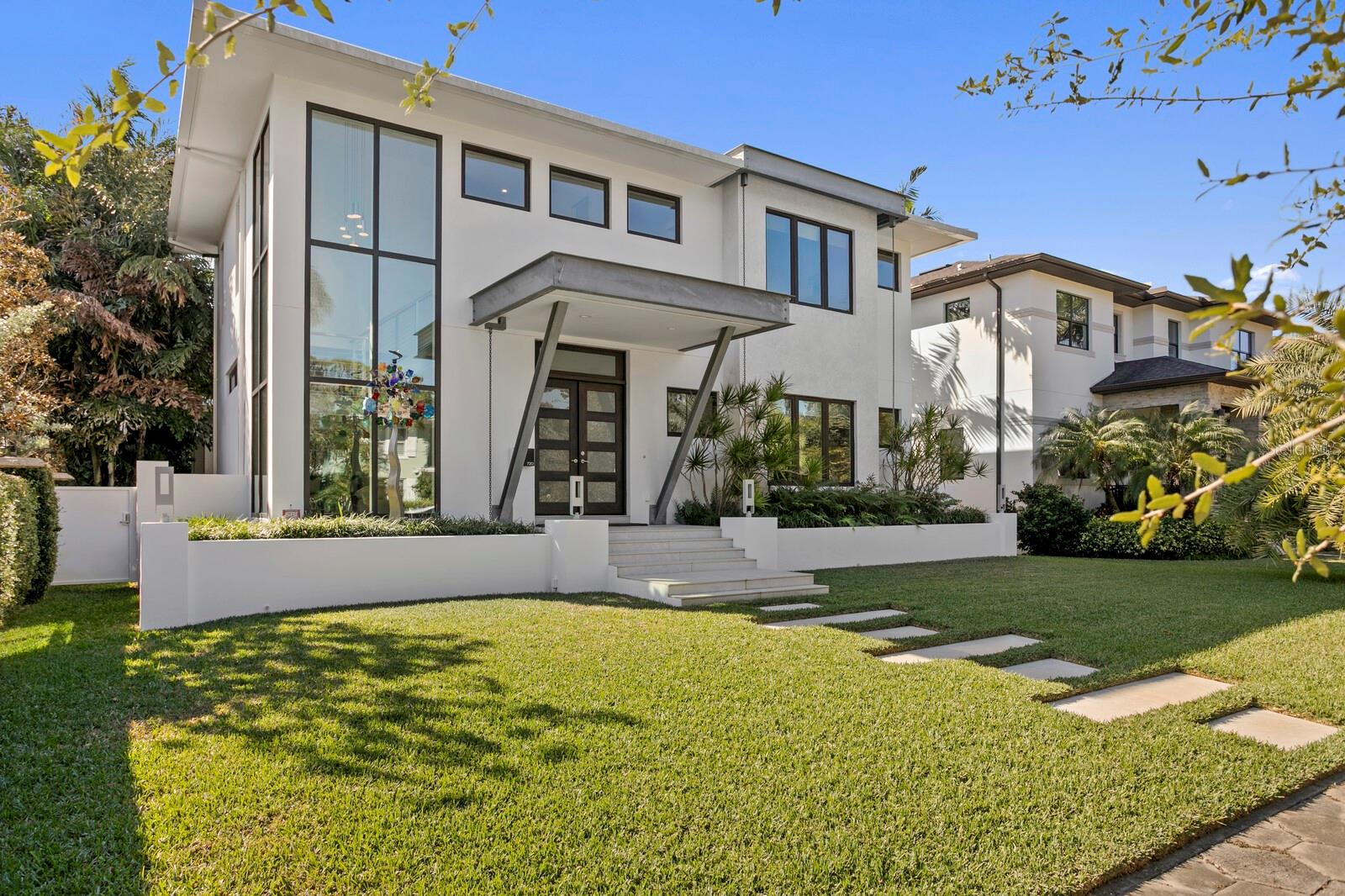 What if you could have modern construction in the hottest historic neighborhood in town? Tree canopies and hex block sidewalks, and holiday spirit beyond imagination? Blocks from the 3rd longest waterfront park system in North America, minutes from vibrant downtown, this “front porch neighborhood” is one of St. Petersburg’s most popular. Step into refined elegance in this custom-built Devonshire home, blending contemporary sophistication with cutting-edge efficiency. Soaring 10-foot ceilings, vast windows, and a striking floating staircase set the tone for the home’s upscale ambiance. The open-concept great room with porcelain tile flooring connects living, dining, and a sleek kitchen that features Thermador appliances, a natural gas cooktop, quartz countertops, a beverage refrigerator, and reverse osmosis water filtration, in addition to a large walk-in pantry. A dramatic live-edge wood dining counter adds warmth and character to the central island. There are four en suite bedrooms, including one on the main level (currently used as an office) that would be ideal for a guest suite. The upstairs primary suite features a luxurious bath with dual vanities, a soaking tub and separate large dual-head shower. There are two large walk-in closets and a Juliet balcony. Two additional bedroom suites are located on this upper level, along with a very functional laundry room. Engineered hardwood flooring on the upper level lends charm to the minimalist style. Step outside to a large covered lanai with a tranquil water fountain, wired and plumbed for an outdoor kitchen. Florida-friendly landscaping and privacy-enhancing masonry walls and vinyl fencing make this a wonderful space in which to relax. Plans for a pool are available, and the oversized 600 sq ft alley-access garage provides ample storage. A spacious mudroom offers even more storage and convenience. Built to current hurricane standards, this home features filled-block construction, Icynene spray foam insulation, a standing seam metal roof, and hurricane-rated windows and doors. Smart home systems include Sonos speakers (indoor and lanai), smart thermostats, Cat-6 wiring, LED lighting, and a dedicated technology closet. A Generac whole-home generator, owned solar panels, and two tankless natural gas water heaters ensure energy efficiency and peace of mind. Located in a neighborhood known for its charm and community spirit—with a voluntary HOA – this is more than a place to live; it’s a place to thrive. Come experience why St. Petersburg makes international headlines as a destination for arts, culture, dining, outdoor recreation and much more.