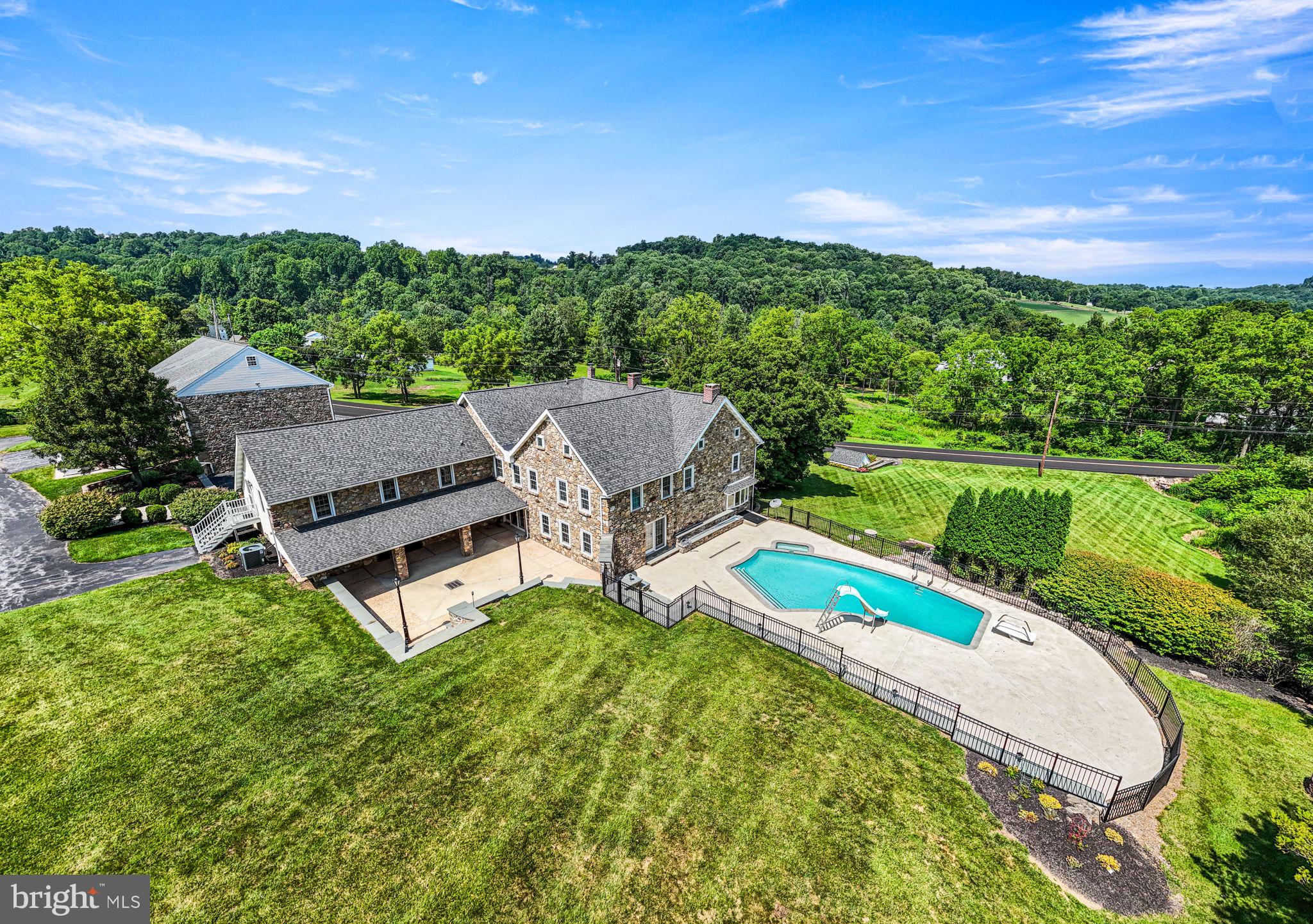 Situated on about 13 scenic acres in the rolling hills just outside of Boyertown, this almost 5000 square foot impressive and expanded stone farmhouse is the ideal homestead for active lifestyles.  Whether you are a car collector, hobbyist, contractor, or gentleman farmer, the huge bank barn, multiple outbuildings, and many garages will give you plenty of space to pursue your ambitions.  The sprawling and updated home, with its beautiful in-ground pool, expansive patios and porches, is perfect for indoor and outdoor entertaining on a grand scale.  Greet guests on an impressive two-story portico. The welcoming floor plan features a huge 40-foot long great room with giant raised hearth stone fireplace, live edge custom bar and cabinetry, bay window, and hardwood flooring. The remodeled kitchen includes quartz counters, tile backsplash, wood floors, double oven, range top alcove, brickwork, a butcher block topped island, and an adjoining breakfast room. A den, entrance hallway, and convenient marble powder room are also located on the ground level. The large second floor is accessed by the home’s original turned staircase, as well as by a stylish modern hardwood curved staircase with wrought iron railing.  This level includes a primary bedroom and en-suite bathroom with walk-in shower, soaking tub, 8’ double vanity, custom tilework; three additional bedrooms; a second full hall bathroom; plus an additional suite of rooms on the back wing to the home.  This bonus suite with two spacious rooms separated by French doors, walk-in dormers, extensive storage, and a powder room could serve as a great home office, guest suite, or recreational activity space. Convenient access to this extra living space can be found via a staircase from the garage, direct access to the second floor, as well as an exterior door leading to the back parking lot.  There is plenty of storage space throughout the home including a walk-up attic and large basement with interior and two exterior entrances.  Parquet wood floors, hardwood flooring, exposed stone interior walls, custom tilework, deep windowsills, and many vintage and historic components add great charm throughout the home.  There is plenty of outdoor space to host large gatherings in the beautiful, partially covered 33’x35’ courtyard framed by flagstone-capped stone retaining walls with built-in bench seating. This area features a unique pebble-finish concrete patio, stone pillars, and barn doors opening to the 3 car garage.  A stone archway leads to the picturesque pool area surrounded by an expansive patio.  The large in-ground pool was just re-plastered and had new coping and tile installed by Anthony and Sylvan pools in July of 2026.  If you are looking for significant storage and workspace for your business or interests, this property has you covered: there’s a 67’x35’ two level, bank barn with two garages on each level. This structure is in great shape and has undergone major renovations.  Other outbuildings include an oversized 39’x19’ garage with a 12’x12’ overhead door; a separate 30’x15’ garage, and charming stone springhouse with water race.  Two large parking lots will accommodate many vehicles. For potential business owners, the township has approved the operation of an owner-occupant’s trade business at this location.  Properties with this combination of beautiful acreage, quality construction, close to 5000 SF of finished living space, extensive custom outdoor hardscaping and entertaining space, and an assemblage of impressive outbuildings are rarely on the market.  Be sure to visit 112 Terrace Road and see all that this spectacular homestead has to offer.