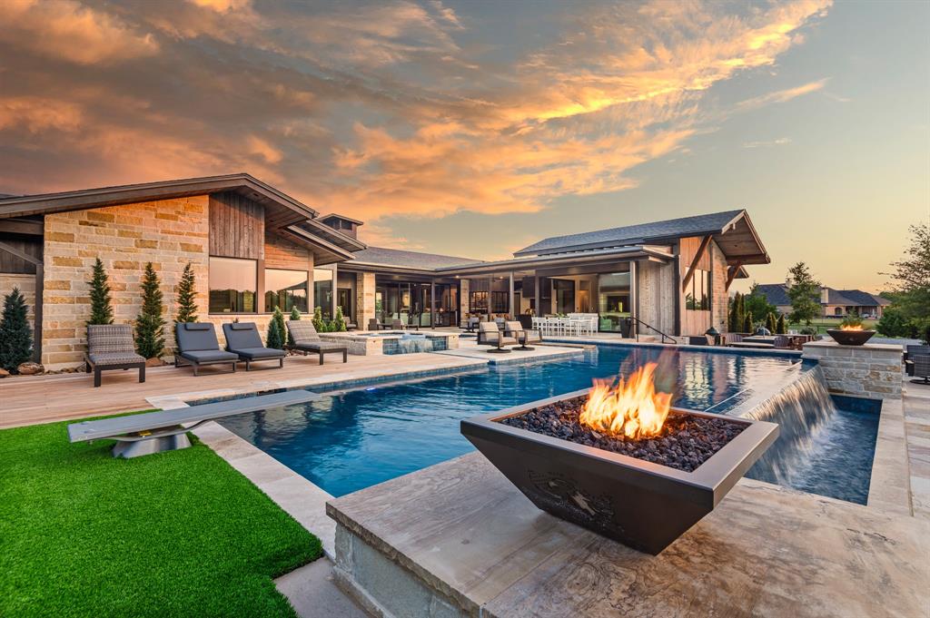 Less than an hour from Dallas, in Rockwall County—Texas’ smallest yet wealthiest county—this lakeside community draws those seeking space, privacy, and an elevated lifestyle. Set on over five acres within a gated subdivision, further secured by its own private entrance, this estate was crafted as the builder-developer’s personal residence and stands as a masterclass in Texas Modern design. Defined by clean architectural lines, organic textures, and expansive walls of glass, every detail is intentionally curated to blend sophistication with ease, offering enriched daily living and effortless entertaining.The 5,649 SF main residence showcases a gourmet kitchen and grand living area anchored by a striking linear stone-framed firebox, where views spill seamlessly outdoors. A dedicated fitness and wellness space opens directly to fresh air and poolside vistas, creating harmony between activity and retreat. From the upper level of the 1,486 SF two-story guest house-design studio, gather next to the fireplace and enjoy sweeping views of the estate and its grounds. The property also includes a 1,497 SF garage with workshop—ideal for creativity, hosting, or collection storage.Outdoor living unfolds across multiple gathering spaces, from expansive covered patios and full kitchens designed for celebrations to sleek lounging areas by the infinity-edge pool with in-pool bar seating. Play pickleball on your private court, watch the kids bounce on the in-ground trampoline, or wander to the private pond where casting a line offers simple joy. Take a ride by horse or ATV on trails within the subdivision. As the sun sets, gather around a fire pit nestled beneath manicured trees by the creek, sharing stories under the Texas sky.This is more than a home—it’s a luxury lifestyle designed for connection, recreation, and retreat. With Dallas less than an hour away, every convenience is within reach while you revel in the privacy of your own sanctuary.