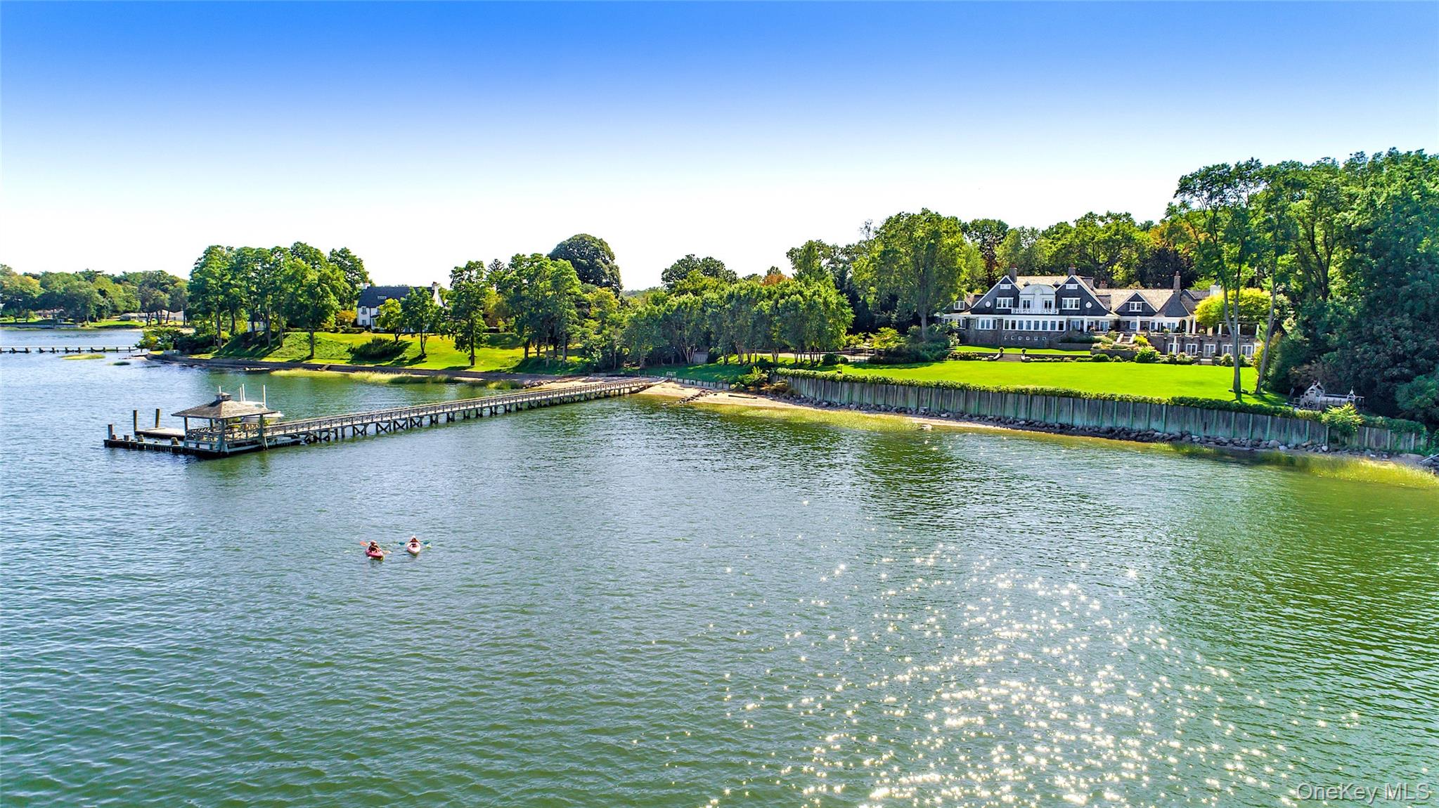 Swan Landing is a magnificent waterfront estate custom-designed by Shope Reno Wharton Associates to exemplify luxury at its highest level. Spanning approximately 23,000 square feet and nestled on 5.4 pristine acres on Long Island’s North Shore, this stone and shingle masterpiece offers 13 bedrooms and 14 bathrooms in a setting of unparalleled beauty and privacy.

A long, tree-lined drive leads past sculpted boxwoods and Tuscan-style columns to the home’s striking facade. Inside, grand barrel ceilings and cove lighting guide you into two formal libraries - one clad in English oak, the other in mahogany - each centered around twin 18th-century fireplaces. The heart of the home, a great stair hall with arched windows and custom inlay flooring, leads into a formal living room with panoramic views of Manhasset Bay, curved window walls, circular columns, and refined finishes. The formal dining room features an antique fireplace, crystal chandelier, French doors, and exquisite custom millwork, flowing seamlessly to a stone patio overlooking the waterfront.

The chef’s kitchen is outfitted with state-of-the-art appliances, a butler’s pantry, a two-level island, and custom cabinetry, while the adjacent octagonal breakfast room - with stained glass accents and five sets of French doors - blurs the line between indoor and outdoor living. Throughout the home, bespoke details abound, from padded and cloth walls to Tischler und Sohn windows, blending old-world elegance with modern comfort.

The primary suite offers breathtaking water views, 12-foot ceilings, a sitting room, and two lavish ensuite baths, one a hand-tiled mosaic showpiece, the other rich in mahogany and emerald green marble. Two walk-in closets with dressing areas and a custom island add to the suite’s refined luxury. Additional amenities on the main level include a refrigerated wine room, antique powder room, a staff suite, and a gated elevator.

Upstairs, two distinct guest wings offer seven bedrooms, five bathrooms, office space, a secondary laundry room, and a heated stone terrace. The lower level features an indoor saltwater lap pool with French doors to the outdoors, a gaming area, temperature-controlled wine cellar, and changing rooms.

The estate grounds, designed by renowned landscape architect Peter Cummin, are a year-round sanctuary with Japanese maples, beech trees, and hydrangea-draped seawalls. Outdoor highlights include a romantic lily pond, English garden, greenhouse, custom pony house, waterfront Har-Tru tennis court, and a private dock and beach with East End-imported sand. An outdoor saltwater pool with slate patio and entertaining pavilion completes the main residence, while a separate two-bedroom, two-bath guest cottage offers additional accommodations.

Grand in scale yet warm in feel, Swan Landing is a one-of-a-kind property where timeless architecture meets modern sophistication - an enduring estate that simply cannot be replicated.