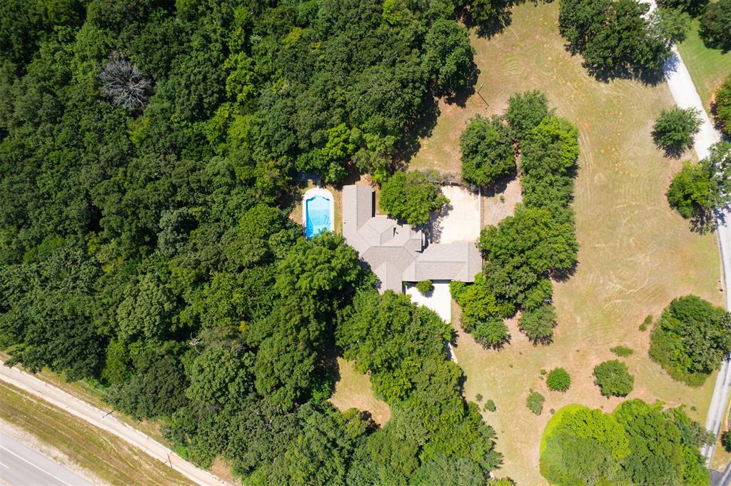 Four wooded acres between Lake Thunderbird and OU. This 4 bed, 4.5 bath home in Hansmeyer Heights offers 4,268 sq ft, a 20x40 in-ground pool, a 4-car garage and a brick porte-cochere on a quiet private street. The fully remodeled kitchen features creme uppers, espresso lowers, a green glass subway tile backsplash, a large curved island with bar seating, black stainless appliances with double wall ovens, floor-to-ceiling pantry cabinets and a window seat with storage. A tiled foyer opens to a formal dining room for 8+, a living room with French doors and a second sitting room. The huge family room has a white plank ceiling, dark beams and a Harmon pellet stove set against brick. The study is lined with built-in shelving. The main-floor primary suite sits apart from the rest of the home with its own wood-burning stove, French doors to the backyard, 2 walk-in closets, a double vanity, garden tub and separate shower. Two more main-floor bedrooms have large closets and access to full baths, plus a half bath and laundry room with utility sink. Upstairs has a bedroom, full bath, large rec room and a wall of built-in storage. Out back: a pool with diving board, a matching 20x40 slab under mature oaks, a covered patio, storage shed and underground storm shelter. A rear motor court with additional garage bays has room for the boat and trailer. Roof replaced 2021 with Class 4 shingles, dual heat pumps, cedar-lined closet, private well and septic. Low $240/yr HOA covers the private streets. Norman Public Schools.