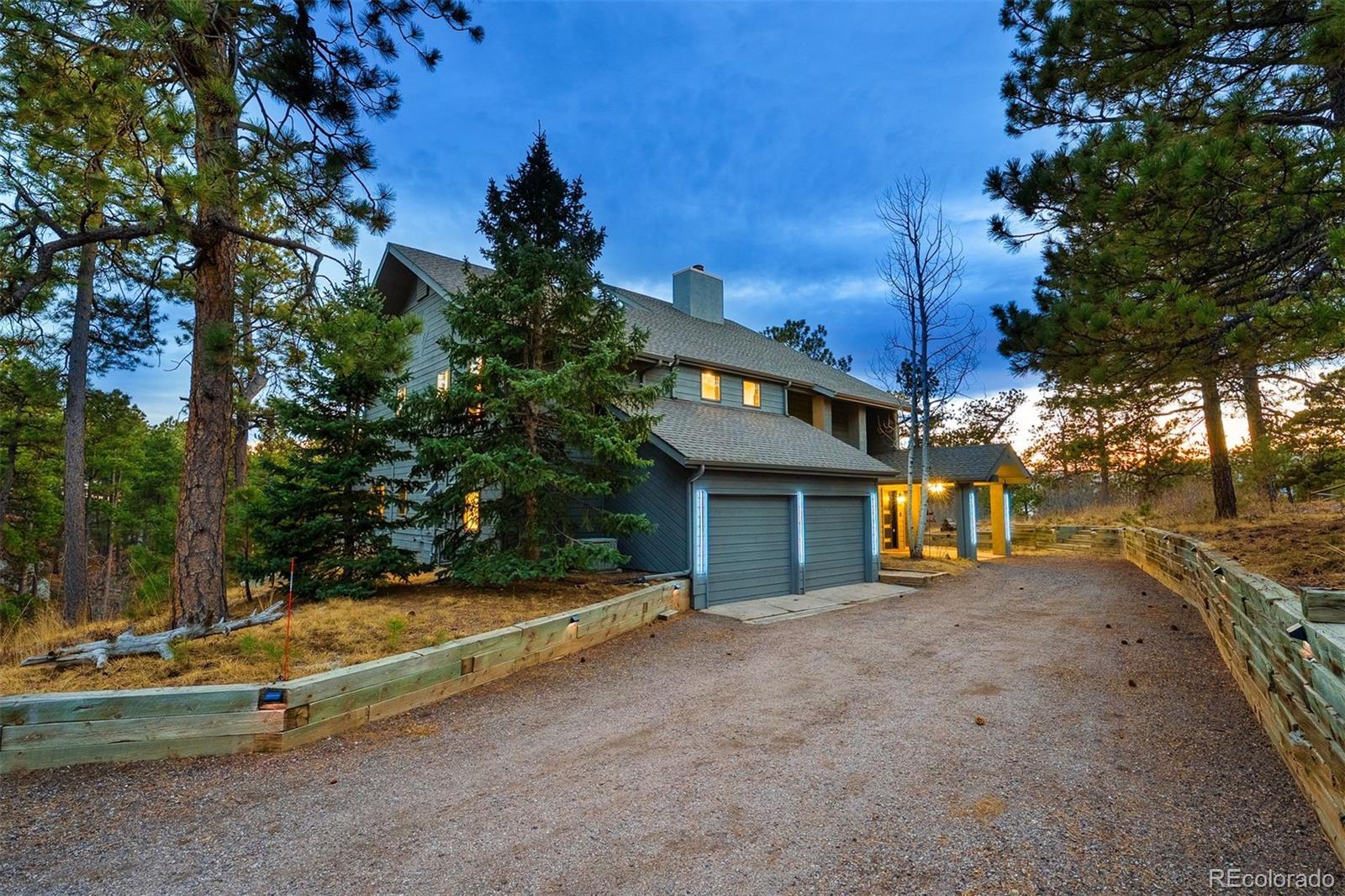 Tucked into the forested hillsides of Woodmoor, this completely reimagined two-story in Monument delivers spectacular Pikes Peak views, a beautifully wooded lot, and a top-to-bottom remodel where modern finishes and natural materials feel at home among the pines and stone of the Colorado landscape. A custom metal entry door opens into a great room anchored by a floor-to-ceiling stone fireplace, 27-foot wood-paneled vaulted ceilings, and a south-facing wall of windows that frame the landscape like a painting. The kitchen, with a six-burner gas range, custom cabinetry, and stainless-steel appliances, lives like luxury. Hickory wood floors run throughout, Dolomite granite countertops ground the kitchen and baths, and details like Carrara marble and Italian glass tile reveal the level of craft woven into every room. Upstairs, the primary suite features a sun-filled bay window alcove with sweeping Pikes Peak views and a spa-inspired walk-in shower with dual rain heads. Just beyond, a library landing offers built-in floor-to-ceiling bookshelves and access to a private deck. Outside, mature pines, natural rock outcroppings, and a wraparound deck with a wood-burning fireplace create outdoor living that feels like a seamless extension of the home. Just minutes from the parks, trailheads, and ponds that define Woodmoor, the Colorado lifestyle is calling.