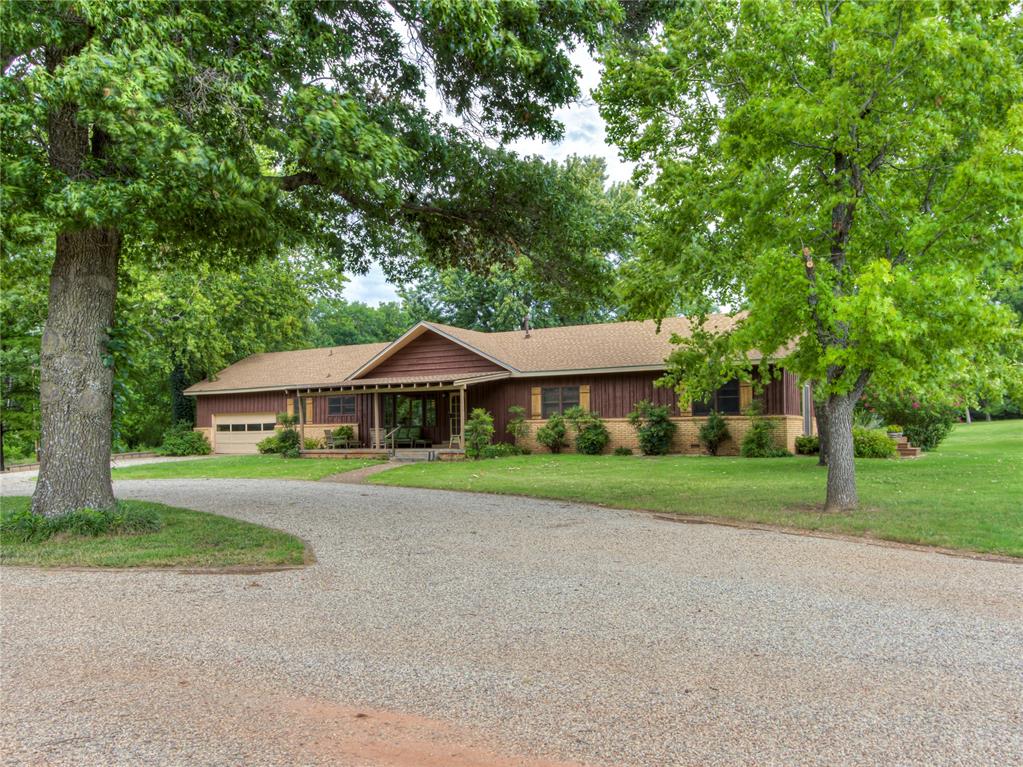 This single-story mid-century ranch sits on 2.55 acres with a large circle drive. All the conveniences of a property in the city with city water, and sewer but with a water well and a bit of room to do what you would like.  A 400 square foot front porch with natural wood posts runs along the front entry. Inside, the 2,234 square foot interior features brand new carpet, fresh paint throughout, and giant room dimensions. The living room centers around vaulted ceilings with mid-toned cedar box beams, a brick fireplace, and multi-pane windows.  The main kitchen is equipped with slate-blue cabinetry, marble-patterned countertops, a gas range, a dishwasher, and a pass-through bar into the dining room. Adjacent to the main living area is a dedicated mud room with an attached half bath. The floor plan includes three large bedrooms and two full bathrooms. The attached garage covers 616 square feet with a two-car entry door, offering space nearly equivalent to a three-car garage.  Outside, sliding glass doors lead to a large back deck and a rock patio featuring a hot tub set beneath a pergola. The barn provides practical space for a workshop, equipment, or animals. Zoned A-2 Rural Agricultural within the City of Norman, the property allows for livestock, outbuildings, and secondary accessory structures. The location combines functional land utility with quick access to local schools, Lake Thunderbird, and the University of Oklahoma.