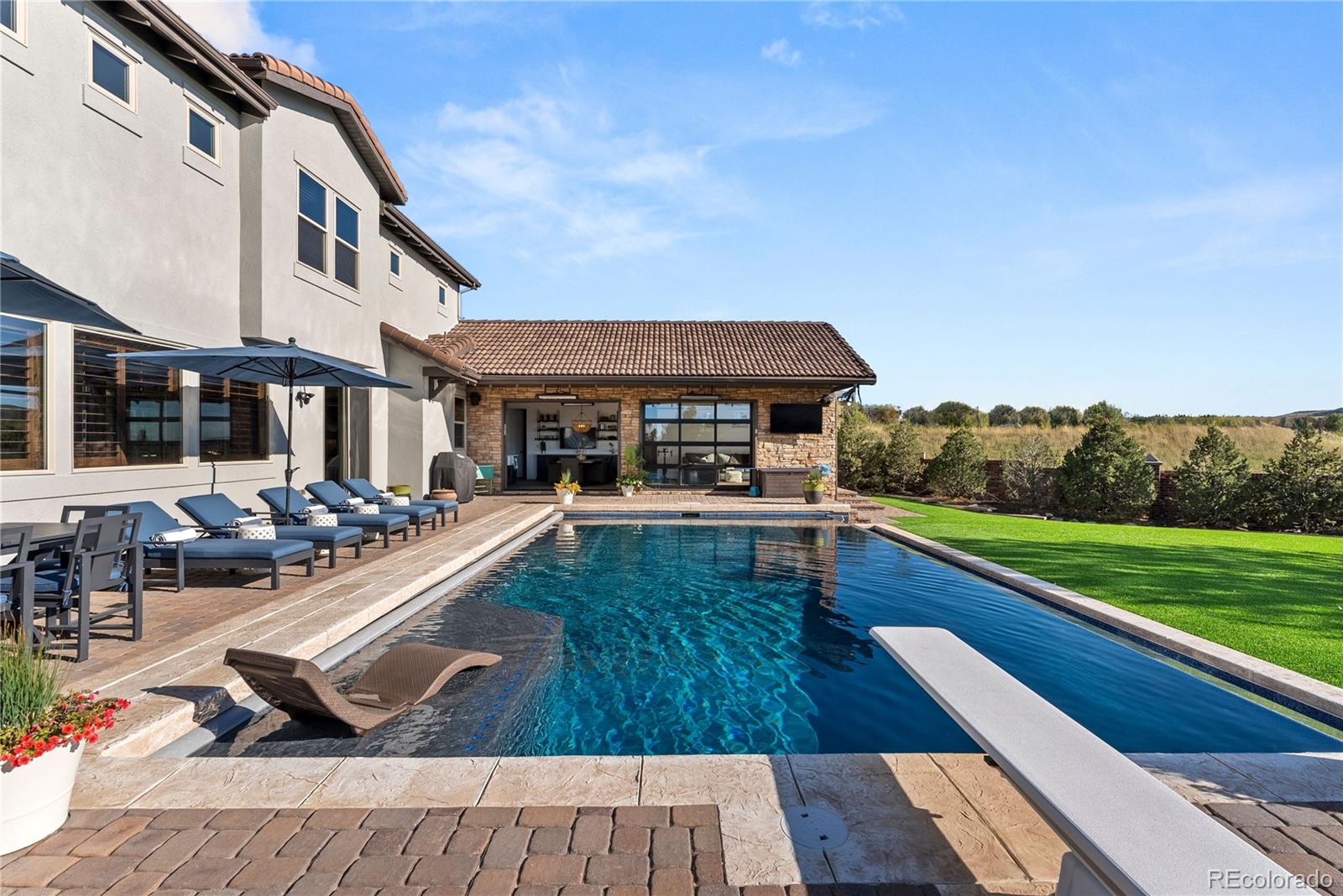 This fully loaded Heritage Hills showpiece offers resort-style living, timeless finishes, and unmatched custom features. Sited on one of the premier lots in all of Heritage Hills, this Overlook residence redefines luxury living with over $1 million in bespoke upgrades and a jaw-dropping pool house addition completed in 2022. Anchored by a resort-style infinity-edge pool and spa, the ADU/pool house includes its own laundry, full bath, wet bar, and HVAC—creating a private retreat that’s as functional as it is stunning. The oversized, West-facing, cul-de-sac lot (originally the highest lot premium in Overlook) delivers commanding mountain views, artificial turf, custom retaining walls, a built-in firepit, and incredible outdoor entertaining space. At the heart of the home is a dramatic central courtyard that connects seamlessly to the interior and offers year-round enjoyment with its built-in grill and custom stone fireplace. Inside, every surface was thoughtfully selected—high-end reclaimed oak floors, knotty alder doors and shutters, rich trim work, and extensive custom cabinetry by Benedettini, Koch, Kitchen Craft, and Decora. The central chef’s kitchen features professional-grade KitchenAid appliances, upgraded quartz countertops, a custom walk-in pantry, butler’s pantry, and even a coveted Scotsman nugget ice maker. The main level also includes a custom office, a huge “project room” with abundant cabinetry, and a unique front entry expansion that allows interior access to both garages—each finished with epoxy floors and custom cabinetry. Upstairs, the luxurious primary suite boasts a private mountain-view deck. Three additional ensuite bedrooms and a spacious loft with custom built-in desks complete the upper level. The finished basement impresses with a 120" theater, decked-out bar, private 5th bedroom, gorgeous full bath, and rare 275 sq ft gym tucked beneath the courtyard. This one-of-a-kind Heritage Hills estate is the ultimate Colorado lifestyle experience.