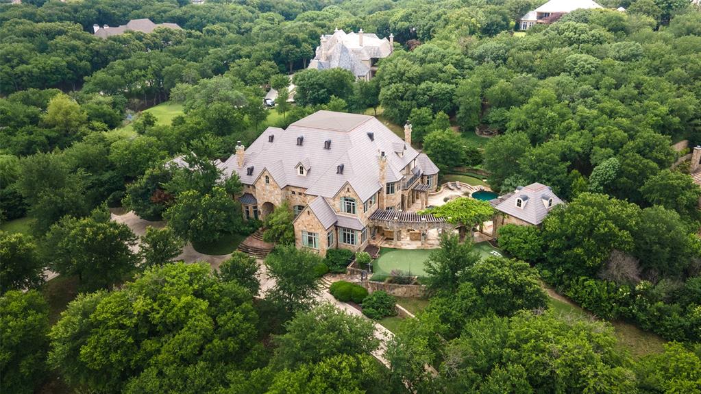 Tucked away on 2.22 private, tree-covered acres within the guard-gated golf course community of Mira Vista, 6901 Sanctuary Lane offers a rare combination of privacy, exceptional entertaining spaces, and everyday livability. Thoughtfully designed for both grand gatherings and intimate family moments, the home features five bedrooms, five full baths, four half baths, four spacious living areas, a private theater, detached fitness studio, pool house, and a six-car garage. The heart of the home is an expansive chef's kitchen that flows seamlessly into the family room, breakfast area, and outdoor living spaces, creating an effortless setting for entertaining. The private primary suite offers a peaceful retreat with a sitting area, spa-inspired bath, and dual oversized closets. The grounds are equally impressive. Resort-style pools and spa, outdoor kitchen, putting green, golf practice area with hitting net, fire pit, and beautifully landscaped terraces create an outdoor environment designed to be enjoyed year-round. Mature trees and rolling topography provide an uncommon sense of seclusion while remaining just minutes from downtown Fort Worth, premier private schools, Clearfork, and DFW Airport via the Chisholm Trail Parkway. Residents of Mira Vista enjoy one of Fort Worth's premier country club communities, recently enhanced by an extensive golf course renovation, along with the security of a guarded entrance and a neighborhood known for its strong sense of community. More than an exceptional residence, 6901 Sanctuary Lane offers a lifestyle where family, friends, and unforgettable moments naturally come together.