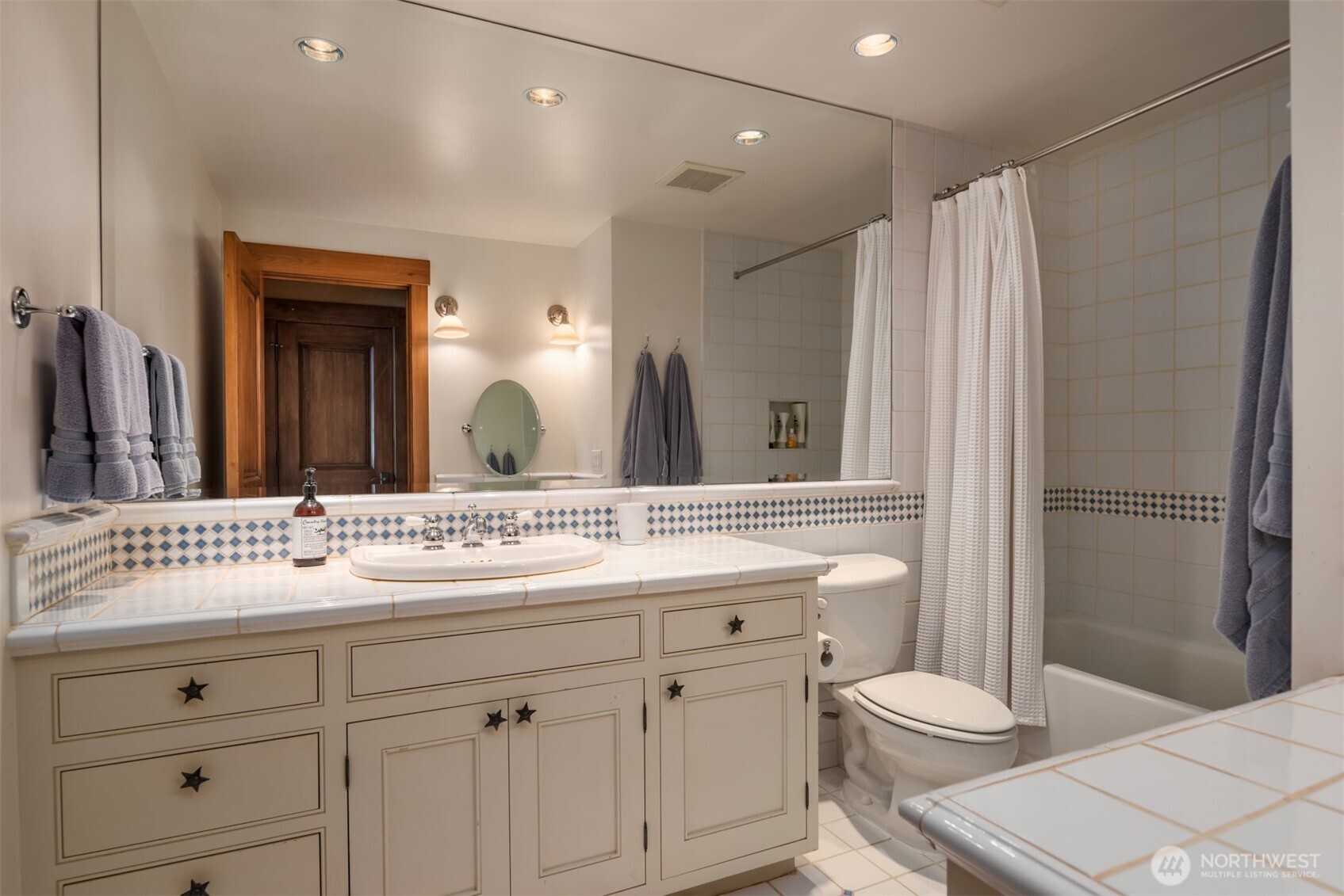 Bathroom with tile countertop, tub/shower combo, and star-accented cabinetry