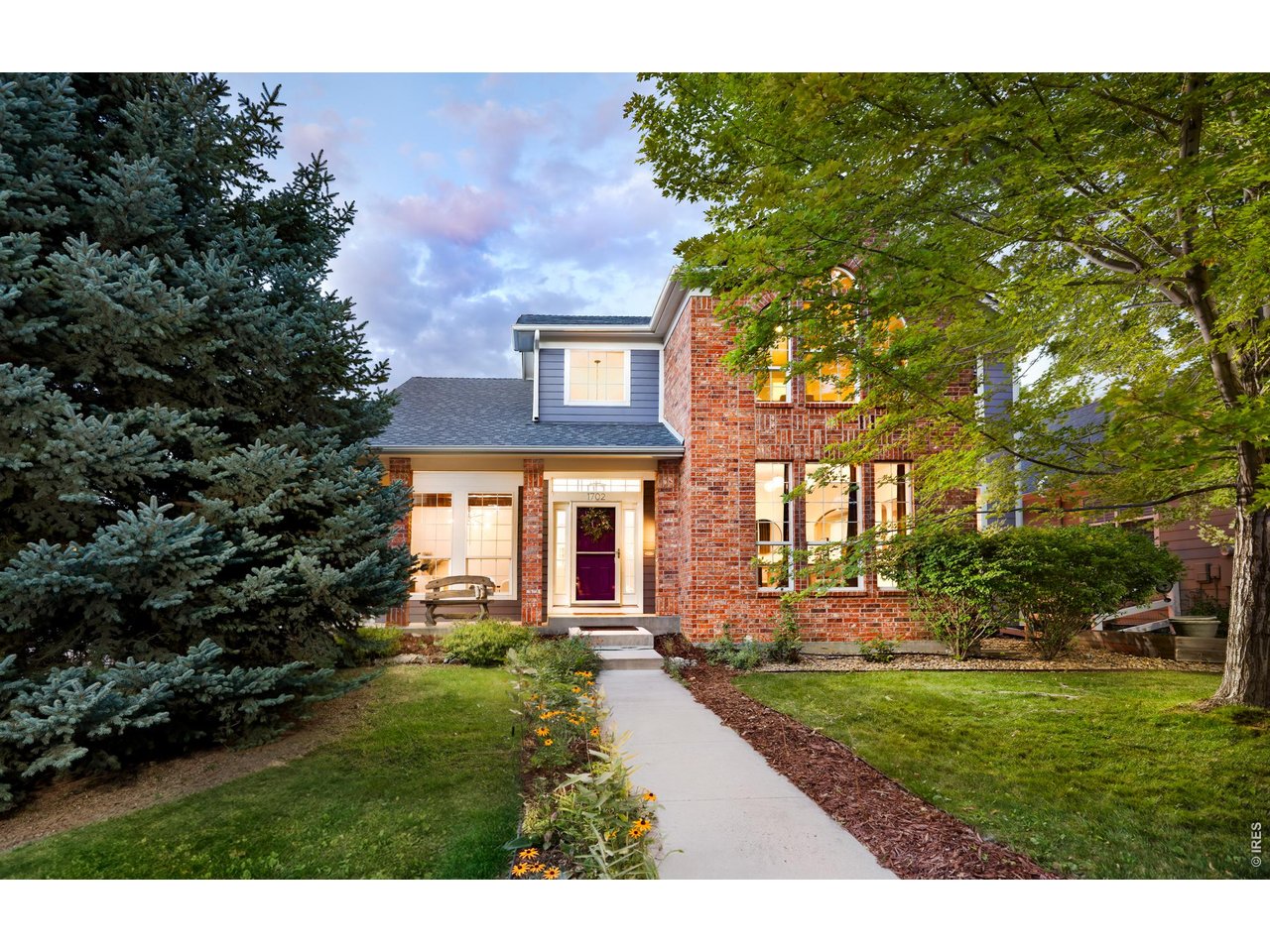 Autumn looks good on 1702 Sicily. A magnificent shade tree brings color to the front yard, tall windows frame the leaves, and a charming community park sits just across the street. On a landscaped corner in southwest Longmont's Renaissance neighborhood, a wraparound porch and established gardens give this home a setting that takes years to grow. The updated kitchen pairs custom soft-close cabinetry and richly patterned stone counters with a curved breakfast bar open to the fireside family room. Warm wood floors, an arched doorway and fresh paint in select rooms complement the bright interior. Out back, the generous deck steps down to a patio and fenced garden beneath mature trees. This is a backyard worth putting your phone away for. All four bedrooms are upstairs, each with a walk-in closet. The vaulted primary bedroom has leafy views, walk-in closet and a remodeled bath with a soaking tub and separate shower. The 1,280-square-foot unfinished basement has lots of possibilities and even a playful streak: its own climbing wall, with space for recreation, projects or future finishing. Summer movies in the park and a neighborhood pumpkin festival add to the seasonal appeal of this location. There is lots to enjoy within a stroll from the house. Schools, trails, coffee shops and restaurants are nearby, with convenient access to Boulder. Schedule a showing today and you'll be home just in time for the holidays.