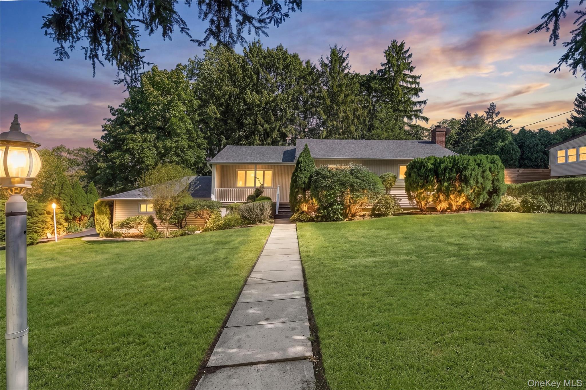 Privately positioned on a corner property in Hartsdale’s sought-after Huntley Estates, locally known as Poet's Corner, this distinctive ranch pairs clean lines with an easy, livable layout and lush, level grounds. A large covered side porch creates an inviting outdoor extension of the home, while inside, the spacious living room and dining area are anchored by a vaulted ceiling, picture window and hardwood flooring throughout. The eat-in kitchen brings a light, neutral palette with crisp cabinetry, granite countertops and a convenient pantry, with a door opening directly to the private backyard. A spacious primary bedroom, two additional bedrooms and a hall bathroom offer a comfortable and functional arrangement. Head downstairs and the possibilities expand, with sliding glass doors opening directly to the backyard, a laundry area, full bathroom and expansive multifunctional space ready for recreation, entertaining or a comfortable lounge complete with wet bar.  The separate outside entrance adds an extra layer of flexibility, making the lower level especially appealing for extended guests or those looking for a more private space within the home. Outside, the expansive driveway accommodates up to six cars, while the corner setting provides generous level grounds and privacy. Close to dining, shopping, schools and transit, this is a Hartsdale ranch designed with flexibility, comfort and everyday ease in mind.