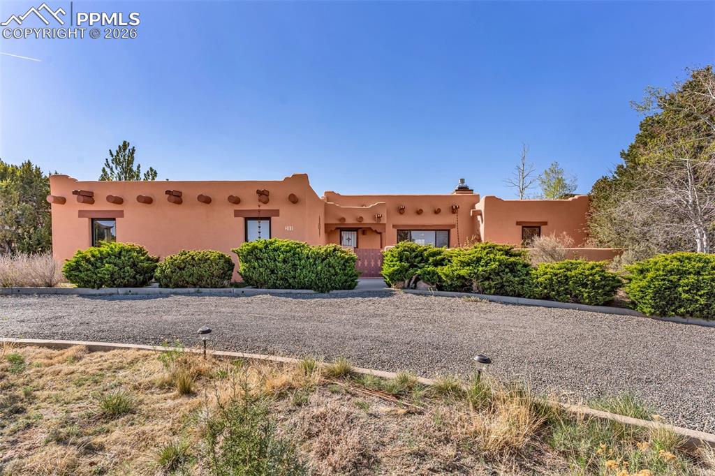 A home that captures the spirit of Colorado living. Framed by expansive skies and sweeping views of Pikes Peak, this Pueblo West residence blends timeless Southwestern design with a setting that feels both peaceful and elevated. The adobe-style exterior and natural surroundings create an immediate sense of place—grounded, warm, and distinctly different. Inside, the architecture does the talking. Exposed beams, soft contours, and a striking corner fireplace bring depth and texture to the main living space. The layout transitions effortlessly between gathering and retreat, with a formal dining area and a curved breakfast nook wrapped in windows that draw in light throughout the day. The kitchen is both functional and refined, featuring granite surfaces, custom cabinetry, and a layout that supports everyday living as easily as it does entertaining. The primary suite offers a private escape, complete with direct outdoor access, a light-filled bathroom, and dual walk-in closets. Two additional bedrooms share a well-positioned Jack-and-Jill bath, while a third bathroom adds flexibility for guests. A separate, oversized living space introduces even more versatility—with its own exterior access and expansive doors, it lends itself beautifully to extended living arrangements, a secondary suite, or a dedicated gathering space with uninterrupted views. Outdoor areas extend the experience, with covered patio space designed for quiet mornings, evening conversations, and everything in between. Homes that combine architectural identity, adaptable space, and this level of setting are not easily replaced.