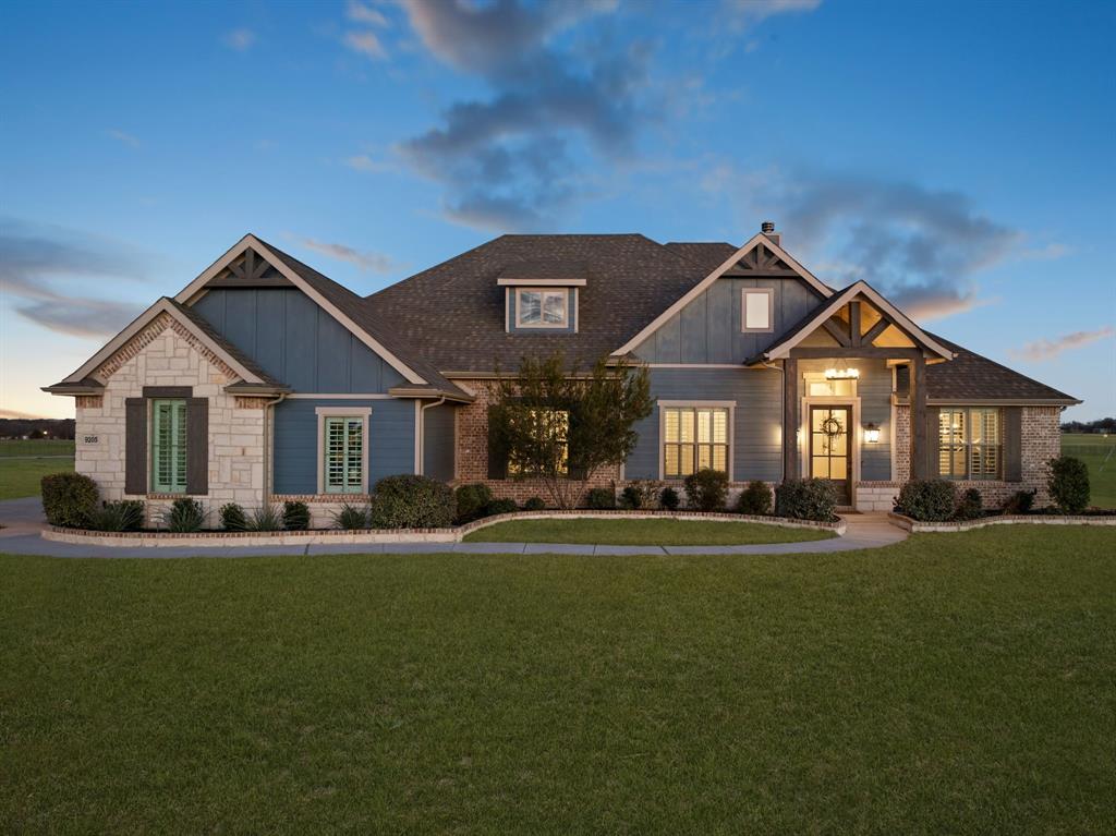 Built by Antares Homes this 4 bedroom 3 bath residence at 9205 Dove Hollow blends modern design with relaxed Texas living on an oversized fenced homesite. Curb appeal shines with a stone plus board and batten facade timber accents manicured landscaping and a sweeping front walk. Inside wood look tile flows through sunlit open spaces. The great room impresses with a vaulted ceiling and decorative beam a wall of windows to the backyard and a dramatic stone to ceiling wood burning fireplace. The adjacent designer kitchen is a showpiece featuring quartz countertops crisp white cabinetry stainless steel appliances pendant lighting a large island with seating and a sizable walk in pantry perfect for everyday meals or entertaining. Plantation shutters and a soothing neutral palette elevate the look. A private study with double doors and a custom accent wall offers an ideal work from home space while a large flex room adapts easily as a media lounge playroom or home gym. Thoughtfully split for privacy the owners retreat boasts a tray ceiling an expansive walk in closet and a spa inspired bath with dual vanities a freestanding soaking tub and a separate shower. Three secondary bedrooms are beautifully appointed each with generous walk in closets and convenient access to two full baths. Outdoor living is effortless on the covered patio overlooking a huge backyard with room for pets play and a future pool. Storage and parking abound with a true three car garage and a gated side drive that leads to a versatile detached metal workshop complete with windows twin covered porches and a concrete slab ideal for hobbies projects or additional storage. Located in desirable Justin moments from dining schools and the Dallas Fort Worth employment corridor this Antares home delivers style flexibility and everyday convenience the perfect place to plant roots and enjoy the best of North Texas living.