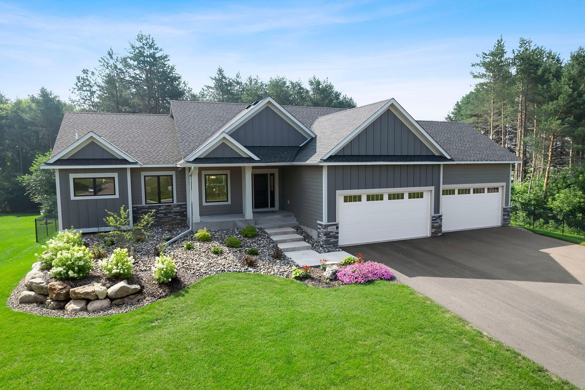 Stunning new 2024-built four-bedroom, three-bathroom rambler situated on over 2 acres of peaceful wooded land in a desirable Ham Lake neighborhood. Just a short walk to Ham Lake Park, the lake, and disc golf course, with easy access to local dining and shopping. This modern open-concept home features luxury plank flooring, stainless steel appliances, custom granite countertops, a farmhouse sink, and a large wood center island with breakfast bar seating. The spacious kitchen includes a walk-in pantry and elegant white cabinetry with under-cabinet lighting. The main level offers a cozy living room with a Heat & Glo fireplace, built-in cabinetry, and large windows overlooking the wooded backyard. A private office/den with double doors, a luxurious primary suite with tray ceilings, dual vanities, soaking tub, walk-in tile shower, and a large walk-in closet add to the appeal. Additional main-level amenities include a laundry room, mudroom with built-in bench and walk-in closet, half bath, and direct access to an oversized, fully insulated four-stall garage. The finished walkout lower level features a spacious family room with gas fireplace, a full wet bar with granite countertops, wine rack, and Sub-Zero refrigerator, plus three carpeted bedrooms and a ¾ bathroom with double vanity. Enjoy seamless indoor-outdoor living with direct access to the large, fully fenced backyard. This home offers a perfect blend of luxury, comfort, and an unbeatable location!