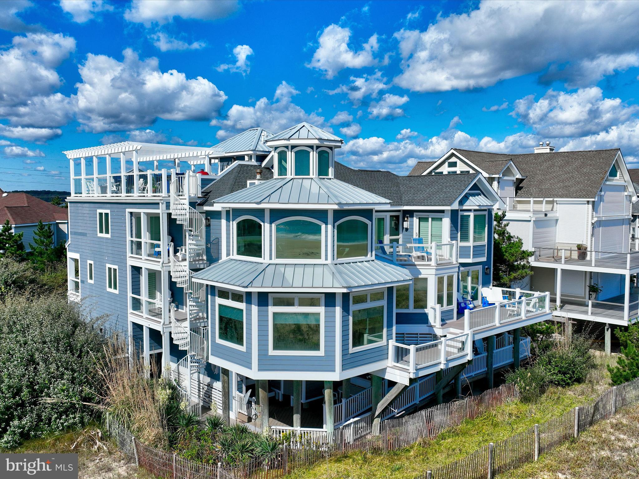 A Castle on the Beach. Discover the coastal elegance of 40110 Owens Court, an extraordinary custom oceanfront home, perfectly nestled beside Fenwick Island State Park. This luxurious coastal retreat spans four levels, offering unparalleled living and entertaining spaces with breathtaking, panoramic views of the ocean, bay, and surrounding wildlife. Updated and expanded in 2017, this home combines modern luxury with timeless coastal charm. Key updates include a new roof, siding, hurricane-proof windows, expanded living areas, and enhanced outdoor spaces, complete with new decking, railings, and an elevator. Designed to immerse you in the beauty of the ocean and bay, natural light floods every corner of the home, creating a seamless connection between indoor and outdoor living. The 2nd floor is a celebration of oceanfront living, where expansive windows and multiple balconies frame the Atlantic’s stunning vistas. At the heart of this level lies the grand living room, crowned by a soaring two-story copula, offering an inviting space for gathering and entertaining while enjoying uninterrupted ocean views. The gourmet kitchen is a chef’s dream, equipped with top-tier appliances including a Wolf stove, Viking fridge/freezer, two dishwashers, and a wine bar. Granite countertops, custom 42" cabinetry, and a sprawling island with generous seating make this kitchen both functional and stylish. Adjacent to the kitchen, a cozy breakfast room offers additional display cabinetry and opens onto the balcony, perfect for morning coffee with ocean breezes. For grander occasions, the formal dining room provides an exquisite setting with the backdrop of the sea, while the family room, doubling as a theater room with surround sound, remote screen, and a fireplace, offers a cozy retreat for movie nights. This level also features two guest bedrooms, each with unique touches and access to private balconies, sharing a well-appointed bath, offering a tranquil retreat for family and friends. The 3rd level is dedicated to two luxurious bedroom suites. The primary suite is a serene sanctuary, complete with an office space, custom cabinetry, a spacious ensuite featuring a dual vanity and walk-in shower, and a private balcony offering serene bay and ocean views. The second suite is equally opulent, with a spa-like bath, access to the main deck, and breathtaking ocean views. A cozy sitting area between the suites provides the perfect nook for reading while surrounded by stunning scenery. Ascend to the rooftop deck and experience the ultimate outdoor living space. Complete with ample seating, a grill, refrigerator, dishwasher, and even a hot tub, it’s an entertainer's paradise. Enjoy the tranquil ambiance of the sunset over the bay, while music from the integrated sound system fills the air. With a half-bath and extra storage on this level, every convenience is at your fingertips. The 1st level of the home offers a separate two-bedroom apartment, each with ensuite baths, a kitchenette, family room, laundry center, and access to the deck and outdoor shower—ideal for guests to have their own private space during their stay. This home also features a handicap-accessible entrance and an elevator, ensuring easy access to many of its living levels. Parking is never an issue, with a beautifully hardscaped driveway that accommodates 8-10 cars, a two-car carport, and elegant landscaping. Located just a short bike ride from the heart of Fenwick Island, you'll enjoy easy access to charming restaurants, boutiques, and entertainment. Come and experience the ultimate oceanfront lifestyle at 40110 Owens Court—where luxury, comfort, and coastal living meet.