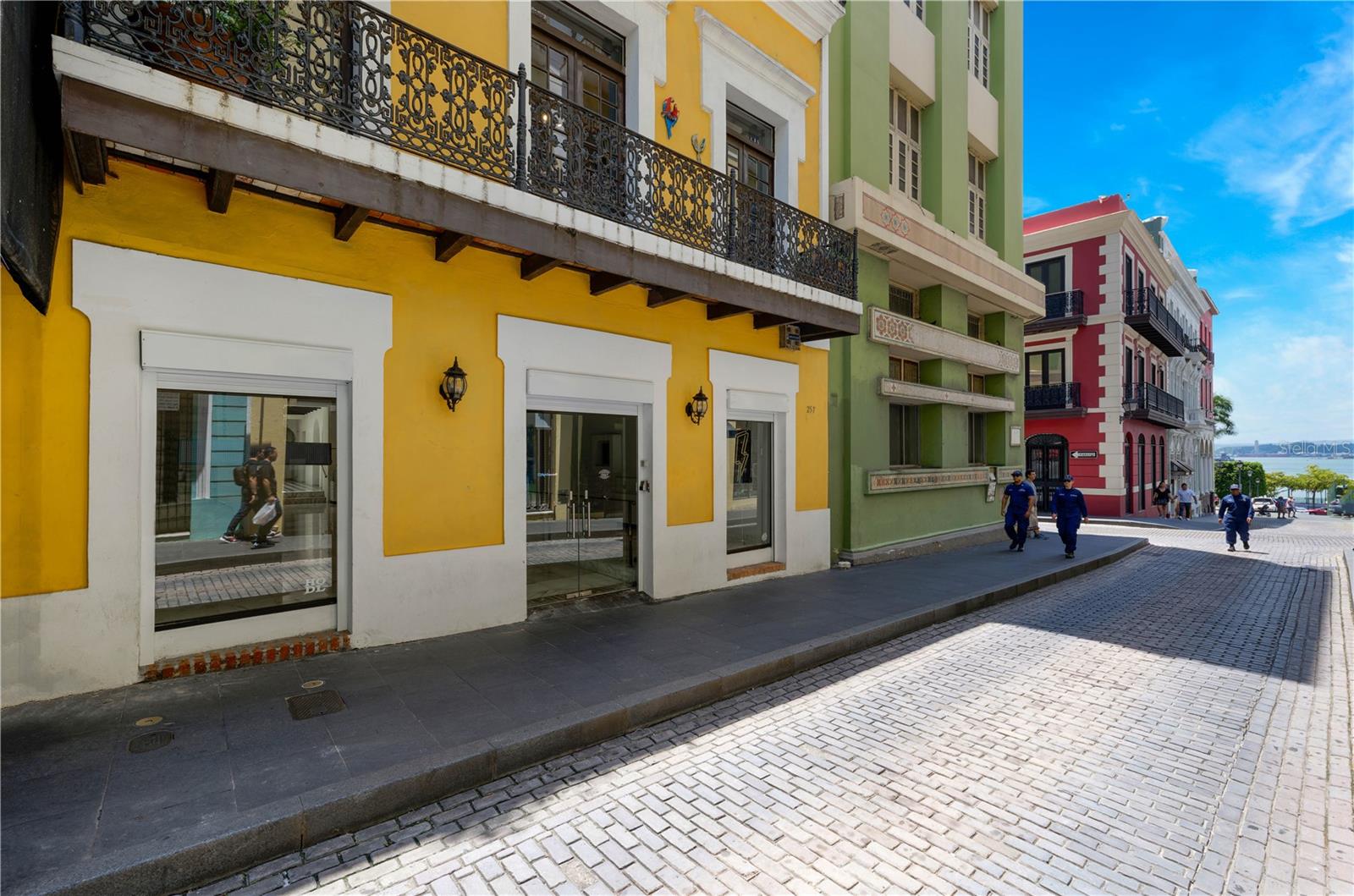257 San Justo Street is situated in the heart of Old San Juan, a historic district renowned for its Spanish colonial architecture and vibrant cultural scene. The area is characterized by its cobblestone streets lined with pastel-colored buildings, bustling with tourists and locals alike. The property, boasting 5,255 sf of air conditioned space, is beautifully maintained with a traditional facade, complete with wrought-iron balconies and street views of San Juan Bay, capturing the essence of Old San Juan’s architectural charm. The first floor showcases an elegant open-concept space with exposed wooden beams, which currently serves as an art gallery. It features refined marble floors and recently renovated powder rooms, providing modern comfort. Further into the space, a stunning interior courtyard is revealed, protected by a skylight roof. The courtyard boasts a captivating fountain, living plant wall, and a full wet bar, making it ideal for a cafe or an entertaining area. There is also a full commercial kitchen in the back that connects to the upstairs, providing the perfect setup for events. The second floor offers a warm, residential feel with the utmost privacy. A foyer leads to the great room, which features wide planked wood floors and a generously-sized layout. Its large windows flood the space with natural light and open up to a balcony that faces San Justo Street and provides partial views of the bay, enhancing the allure of this one of a kind offering. There is also potential to create a rooftop area, adding even more versatility to this unique property. The neighboring property, 255 San Justo Street, is also available for purchase at $849,000.