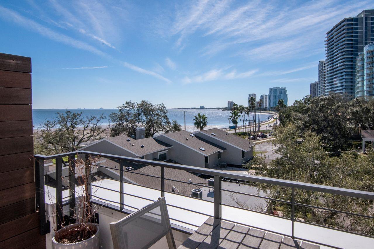 Welcome to this exceptional modern townhome just steps from the iconic Bayshore Boulevard, where refined design meets an unparalleled Tampa lifestyle. Ideally situated within the coveted Plant High School district, this four-story architectural masterpiece offers 3,607 square feet of heated living space and 5,034 total square feet under roof, featuring three bedrooms, office, three full baths, and two half baths, all finished with meticulous attention to detail. From the moment you arrive, the home’s striking modern façade and expansive impact-rated windows and doors set the tone for the elevated living experience within. Upon entry, it is immediately evident this is no ordinary townhome. The first level features a private guest suite with solid wood flooring and a beautifully appointed en-suite bath showcasing a floating vanity, marble countertops, and a tub/shower combination with seamless glass enclosure. This level also offers direct access to a fenced outdoor area. A spacious hallway with three closets and elevator access completes the floor. Ascend via the elevator or the dramatic staircase with sleek modern railings to the second level, where a breathtaking great room awaits. Solid wood floors flow throughout the expansive space, enhanced by designer lighting, a custom accent wall, built-in surround sound, and motorized shades. The great room opens to a large covered porch with stunning bay views, creating a seamless indoor-outdoor living experience. A custom built-in cabinetry system with quartz countertops and dual wine refrigerators adds both function and sophistication. At the heart of the home is the custom-designed chef’s kitchen, featuring exquisite cabinetry, a substantial waterfall-edge island with ample seating, leathered stone countertops, designer backsplash, and top-of-the-line appliances, including a Sub-Zero refrigerator and JennAir and Wolf appliances. A conveniently located half bath sits just off the kitchen. The third level hosts the serene owner’s retreat and an additional bedroom, both featuring solid wood flooring and custom accent walls. The primary suite is a true sanctuary, offering motorized blinds, dual custom walk-in closets, and a spa-inspired bath with a floating double vanity with marble countertops, an oversized walk-in shower with rainfall, handheld, and fixed shower heads, a freestanding soaking tub, seamless glass enclosure, and a private water closet. The secondary bedroom includes a generous closet and a beautifully finished en-suite bath. The pinnacle of the home is the fourth level, where two expansive rooftop terraces deliver breathtaking views of Tampa Bay and Bayshore Boulevard. The south-facing terrace features a built-in gas grill, while the expansive north-facing terrace—mostly covered—offers a built-in outdoor kitchen with stone countertops, refrigeration, and storage, ideal for year-round entertaining. This level also includes a private office with custom built-in cabinetry and an additional half bath. Additional upgrades include a electric outdoor fireplace, motorized blinds on the first three floors, accent walls, shower water filtration, and wired Google pods on every floor. Perfectly positioned within walking distance to premier dining and nightlife, including Maru Rooftop, Barcelona Wine Bar, and many more. This remarkable townhome offers modern luxury and an unbeatable location—just minutes from downtown Tampa, Hyde Park, and world-class shopping, dining, and entertainment.