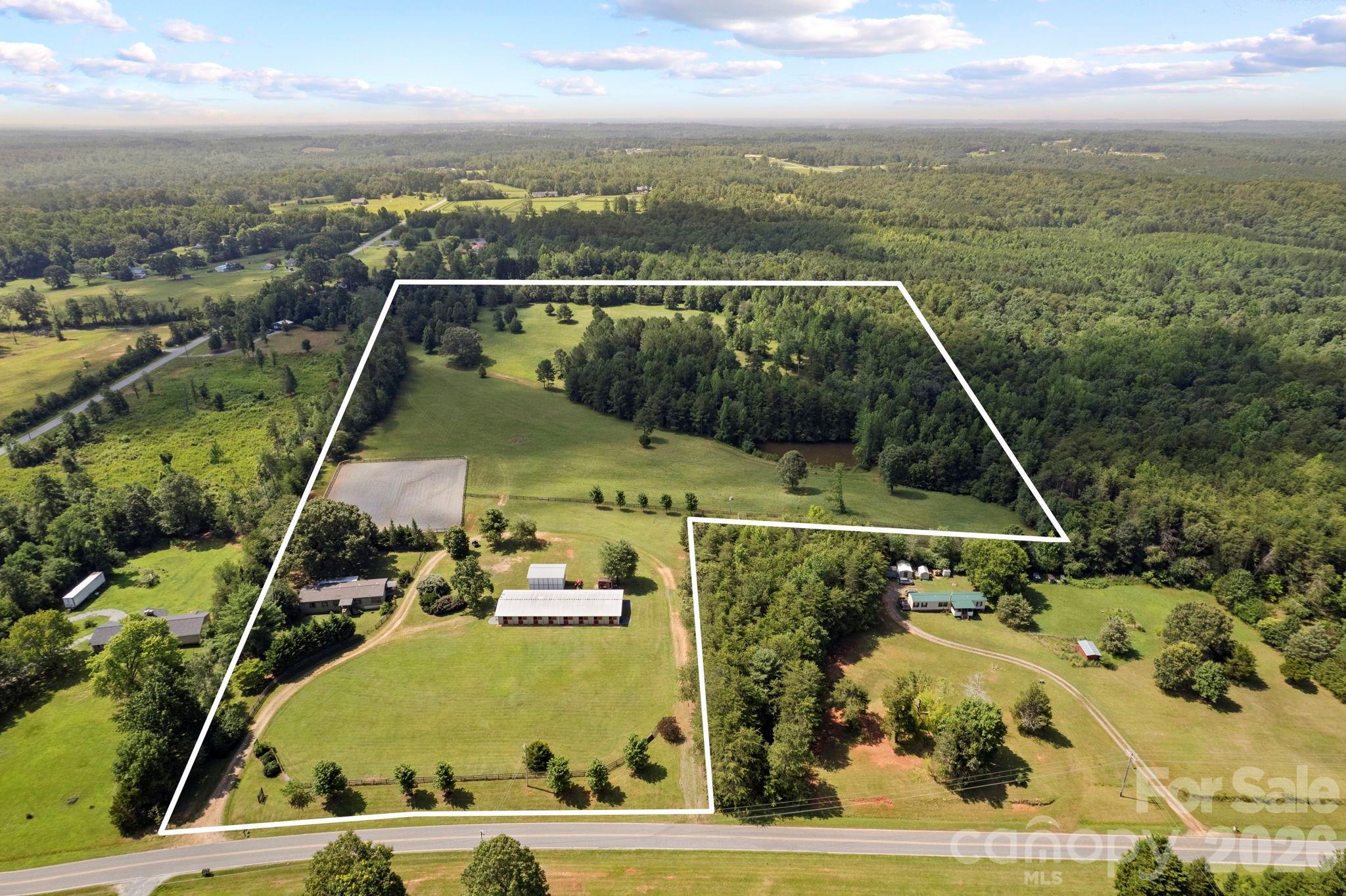 Equestrian alert! 25-acre horse farm with 10-stall barn and riding arena. The property includes a 3BR/2BA manufactured home remodeled with rustic overtones, featuring an open floor plan, ensuite primary bedroom, wood burning fireplace in living room, and a delightful back covered porch area. New HVAC, roof and well pump within the last 10 years. The home is perfect for anyone with simple living needs, or to use while constructing a larger home on the property, then perhaps later as a guest house. Equestrian amenities include a 10-stall center aisle barn with wash stall, tack room, feed room, laundry, bathroom and fly spray system. On the grounds, a 150x200 riding arena, 5 fenced paddocks, over 10 acres of well-established open pasture for hacking, additional fencing, and/or additional home site(s) - for which there are several great spots. 20x30 multi-purposed shed for equipment, hay, shavings, etc. RV hookup with power and septic. Large circular driveway for easy trailer in and out. Perimeter fencing. Automatic main entrance gates. Beautiful, picturesque landscapes include rolling fields, a variety of trees, and a pond. 10 minutes to Tryon International Equestrian Center. Perfect for a trainer, private equestrian with several horses, or anyone seeking a large property with the option to build more. Lots of possibilities with this one!