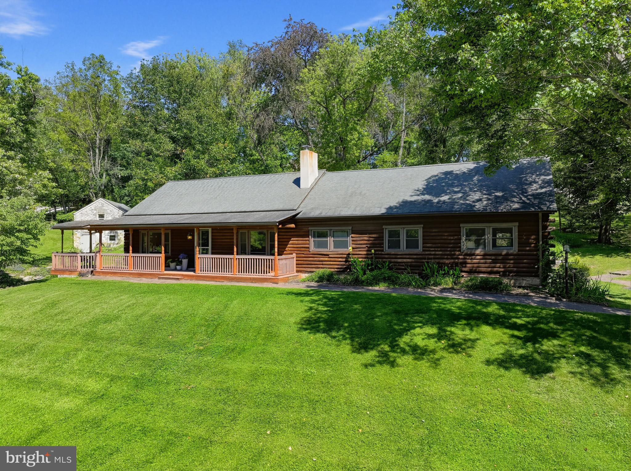 Welcome to this charming 3-bedroom, 2-bath log home situated on 1.2 picturesque acres just around the corner from Marsh Creek State Park. Rich in character and history, the property features a remarkable late-1700s two-story spring house, a peaceful spring-fed pond with sitting area, and a historic stone barn foundation that creates a unique backdrop for outdoor entertaining. Inside, the impressive great room features a vaulted ceiling with exposed wood beams, a cozy wood stove, and an open layout connecting the living, dining, and kitchen areas. The kitchen offers granite countertops, an island with seating, and updated appliances. A bright sunroom provides the perfect place to relax and enjoy views of the surrounding property. The home offers three bedrooms and two full baths, including a primary bedroom with private bath and walk-in shower. A finished loft overlooking the great room provides additional flexible space for a home office, studio, or storage. The basement offers laundry and additional storage, while updated windows and doors enhance comfort and efficiency. A second driveway leads to a detached three-car garage with carport, ideal for vehicles, hobbies, or additional storage. With 1.2 acres of tranquil surroundings and Marsh Creek State Park nearby, this distinctive property offers a wonderful combination of history, nature, privacy, and rustic charm.