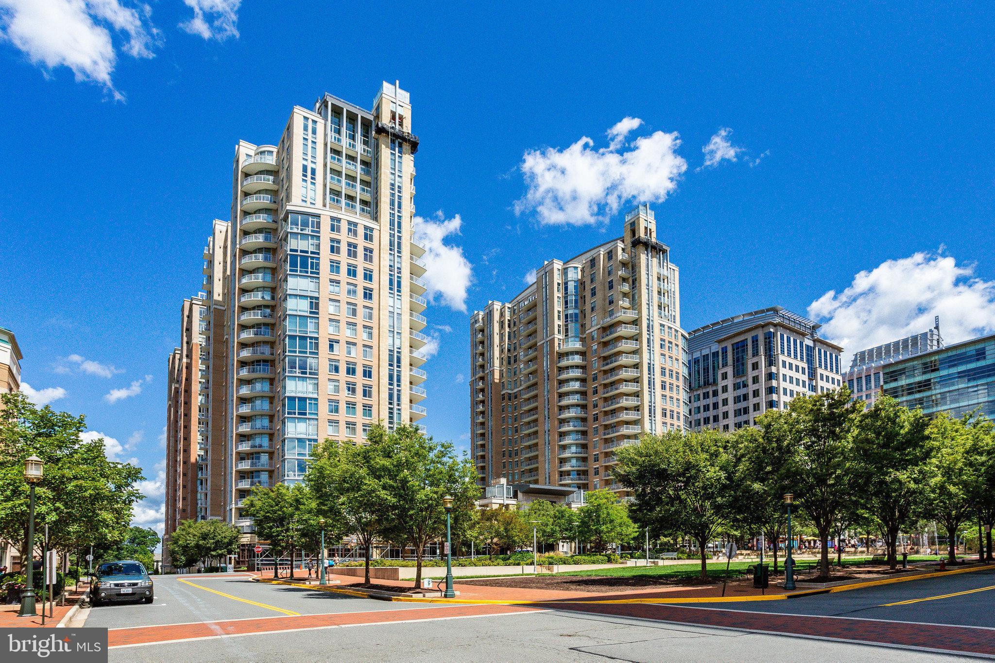 A rare opportunity to own a two-level penthouse in the coveted West Tower at Midtown—Reston Town Center’s premier luxury address—offering nearly 3,000 square feet of elevated, low-maintenance living designed for those who demand both sophistication, privacy, and efficiency. With 4 bedrooms, 3.5 baths, expansive private terraces, and an exceptional 5 dedicated parking spaces, this residence delivers the scale of a single-family home with the ease of a full-service, lock-and-leave lifestyle. Soaring two-story ceilings and floor-to-ceiling windows define the main living space, flooding the home with natural light and creating a dramatic, modern aesthetic. The open-concept layout seamlessly connects the living and dining areas to a private balcony—ideal for entertaining or unwinding between travels. The chefs kitchen is built for both performance and style, featuring a large island, premium appliances, extensive cabinetry, and a built-in workspace—perfect for remote work, tracking your portfolio, or managing business on the fly. A secondary lounge or dining area with a beverage fridge adds flexibility for hosting or everyday living. Upstairs, the penthouse experience continues with vaulted ceilings and two expansive terraces offering elevated views and multiple outdoor living zones—perfect for morning coffee, evening cocktails, or private downtime above the city. The primary suite functions as a true retreat, complete with a spa-inspired bath, dual vanities, soaking tub, and frameless glass shower. Additional bedrooms on the main level provide versatile space for guests, a home office, or a private fitness setup. Smart, integrated features—including built-in audio, remote-controlled shades, and modern lighting—enhance comfort and convenience while maintaining a clean, contemporary design. Midtown delivers a full-service, executive-level lifestyle with 24/7 concierge, secure access, and resort-style amenities: a heated outdoor pool and hot tub, state-of-the-art fitness center, private theater, conference facilities, guest suites, and elegant entertaining spaces. On-site dining and package handling ensure seamless day-to-day living, while the vibrant energy of Reston Town Center—top-tier restaurants, nightlife, and transit—is just steps away.  10 minutes to Dulles International Airport.