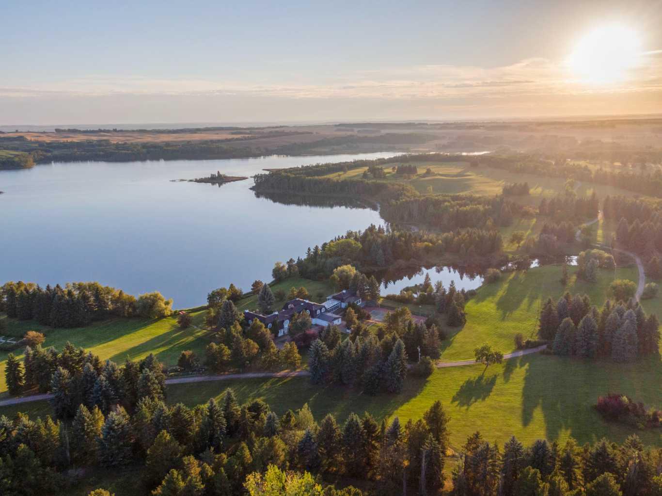 Located in the quiet, picturesque countryside of Lacombe County, the Gadsby Lake Estate is a once in a lifetime opportunity to own a secluded paradise offering just about everything you can dream of. Opulent architectural features and exquisite design elements are found throughout both the main residence and adjacent lodge, including the use of one-of-kind building materials from around the world. In addition to the 17 bedrooms and 31 bathrooms, this stunning estate boasts several specialty rooms including a library, a bright and airy atrium, a sauna and gym, large wine cellar, an indoor pool and lounge, a grand party room, private theatre, and games room. Each space is impeccably designed with elegance, comfort, and convenience in mind. Beautiful windows and outdoor seating lounges, deliver both spectacular lakefront views, and a feeling of tranquility and connection to the serene natural surroundings. Gorgeous stone fireplaces, rich wood accents, and suite-style guest quarters with spa-like ensuites create a warm, welcoming environment for owners and guests alike. A multitude of recreational amenities just for you can be found throughout the Estate’s almost 300 acres. Hiking, fishing, canoeing, and  tennis courts are just some of the activities that can be enjoyed in the utmost privacy., whenever you’d like. The property also features paved and natural pathways through seemingly endless secluded parkland. Rolling hills, elaborate landscaping and lush gardens create an oasis unlike any other you’ll find in Canada.