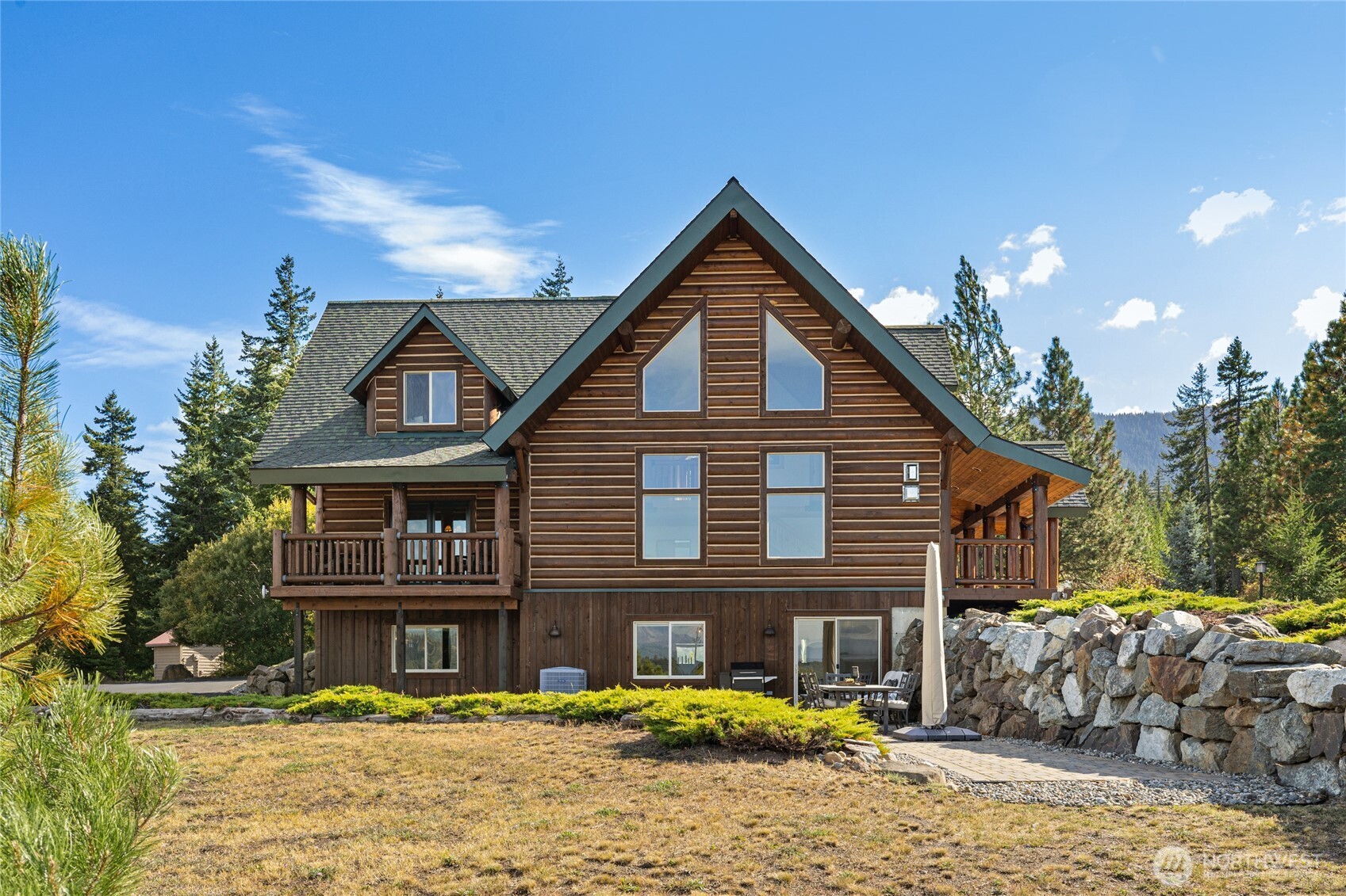 Rear exterior showcasing the home’s log construction, multiple covered decks, and lower-level patio.