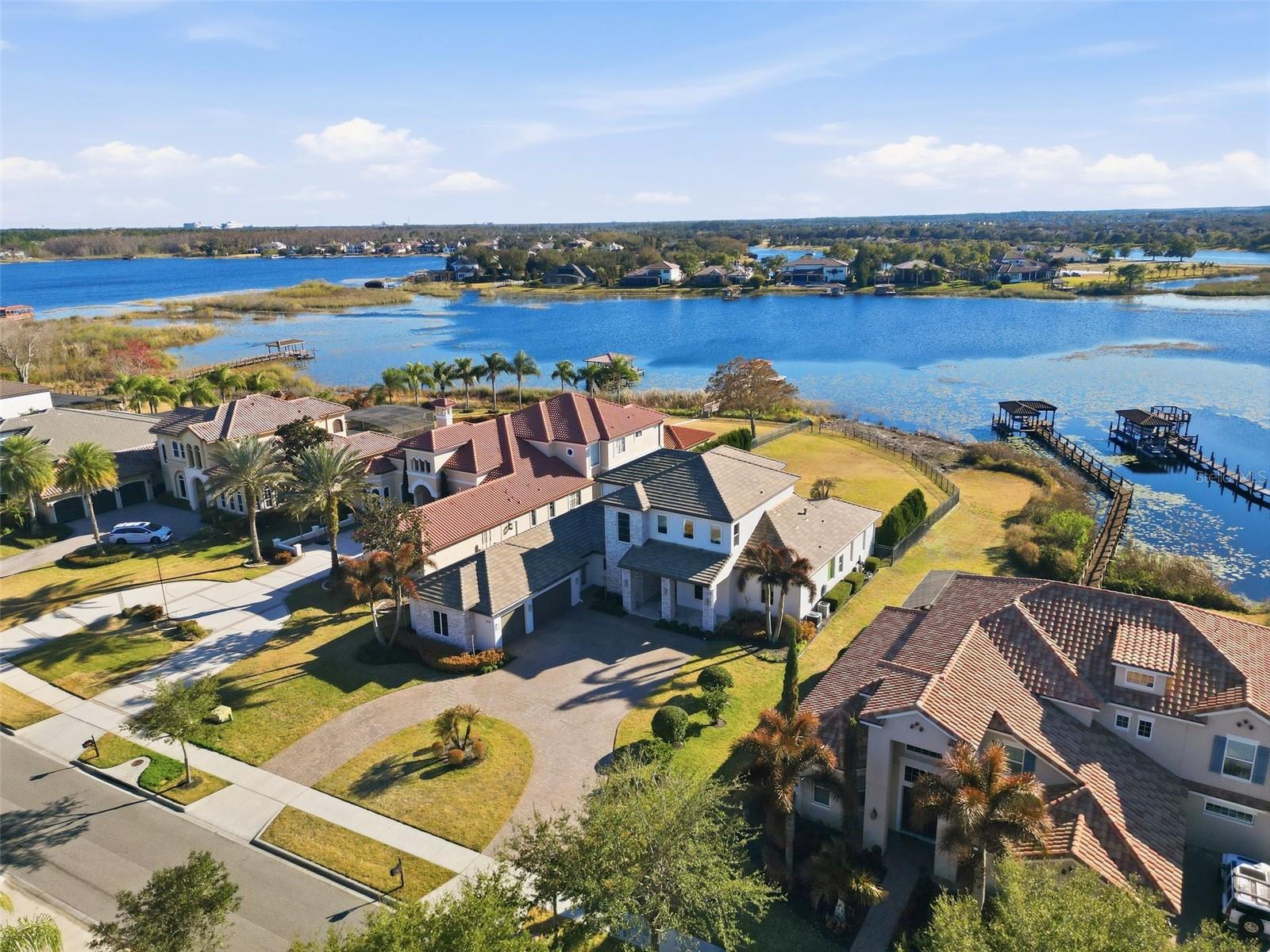 Luxury meets laid-back lake living on Lake Hancock in Winter Garden, inside the sought-after Independence community with parks, trails, and a true neighborhood feel. Custom built by Brierhill Homes, recognized as MCBC Builder of the Year, and professionally designed/furnished by Gilmore Design Co., this exceptional direct lakefront residence sits on one of the area’s largest lots—with an oversized, fully fenced backyard—perfect for entertaining—where you can enjoy stunning sunsets over the water and catch the Disney fireworks on select nights. Arrive via an impressive circular drive and step into a striking entry featuring a custom front door, polished natural stone flooring, and a dramatic stone accent wall—framed by a deep, covered front porch with a rich wood-plank ceiling that immediately sets the tone. It’s a welcoming space that’s perfect for a small seating area to enjoy morning coffee or greet guests in style. Inside, the home is bright, elevated, and designed for both entertaining and everyday comfort, highlighted by a timeless coastal-modern palette with white oak flooring, a beautiful white oak staircase with integrated LED lighting under each step, and custom ceiling details throughout (including soffit/tray accents and integrated lighting). The layout offers 5 bedrooms, each with a private en-suite bathroom and walk-in closet, and each bedroom includes blackout honeycomb shades for comfort and privacy—including a stunning first-floor primary suite with serene lake and backyard views, plus a dedicated first-floor guest suite. You’ll also love the private office and a media room that easily works as a flex space (playroom, gym, second lounge, or homework room). At the heart of the home, the chef’s kitchen showcases Thermador appliances and a show-stopping double island topped with Cambria quartz with subtle gold veining, plus a custom chevron-designed backsplash with under-cabinet LED lighting that highlights the detail beautifully. The kitchen flows seamlessly into the main living space for true indoor-outdoor living. A wall of living room sliding glass doors opens wide, creating one expansive space that connects the interior to the lanai, pool, and lake beyond. Enjoy built-in Sonos sound in the living room and kitchen, with audio extended to the outdoor kitchen as well—plus the flex/media space is pre-wired if additional speakers are desired. The living room also features a sleek gas fireplace framed in natural stone, flanked by custom built-ins for a clean, designer finish. Out back, unwind in your private retreat with a heated pool and spa, generous covered areas, and a summer kitchen made for sunset dinners. The first-floor lanai (including the summer kitchen) and the second-floor balcony are both fully encapsulated with motorized screens controlled by remote—perfect for effortless, bug-free evenings and both outdoor living areas feature a warm wood-plank ceiling accent that brings a high-end, resort feel. Additional highlights include a whole-home water softener/filtration system (low/zero maintenance), a built-in security system with exterior cameras, built-in Sonos audio, and whole-home smart lighting with keypad controls and scene presets—plus an oversized 3-car garage. Select furniture may be purchased separately upon request.