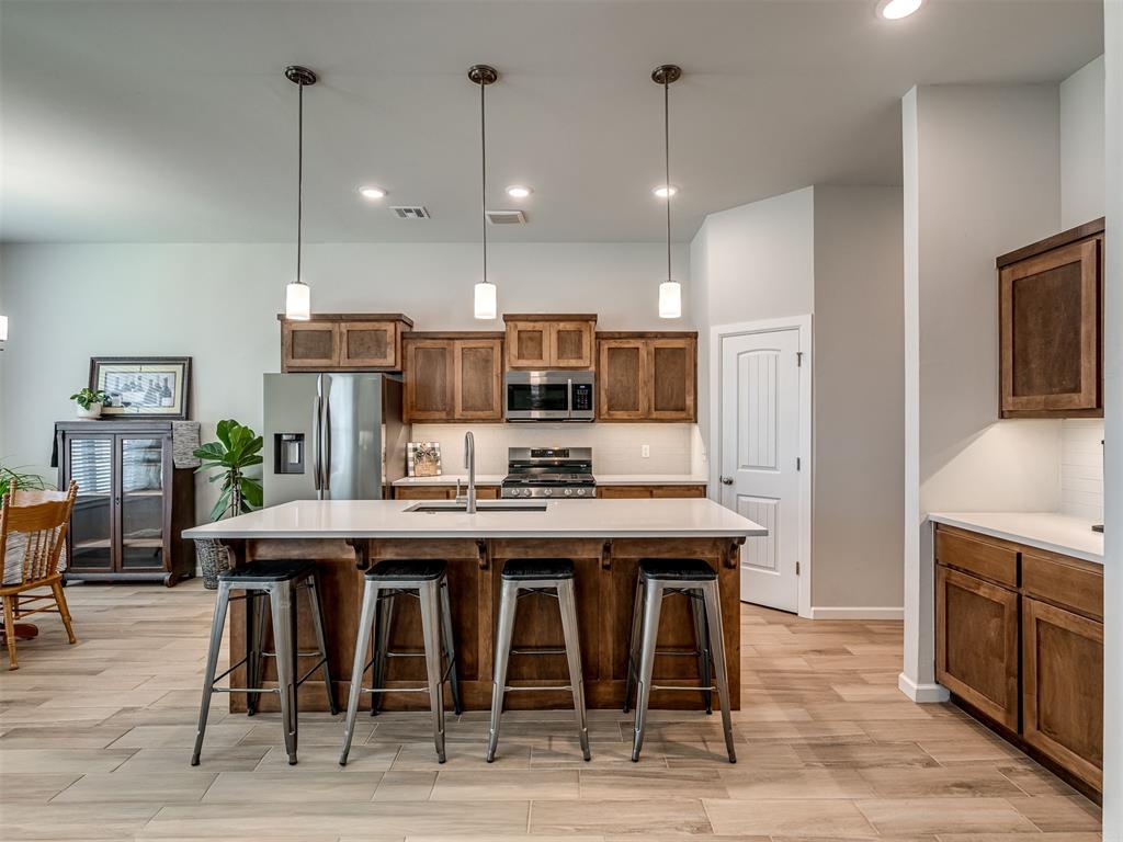 Sophisticated style and thoughtful details define this nearly new, two-year-old home featuring 3 bedrooms, 2 baths, and a dedicated office. This kitchen is a showstopper with its country pine cabinetry, a designer upgraded backsplash, ample cabinet space, walk in pantry and seamless flow into the living and dining areas, ideal for entertaining and everyday living. Living room is oversized with gas log fireplace and the sliding barn door adds character to the large private office right off the living. The open-concept floor plan feels spacious and inviting, with wood-look tile flooring throughout the home for a warm, feels like home finish. This Mother-in-law floor plan puts the primary and additional bedrooms on opposite sides of the the home. Primary bath has double vanities, fully tiled shower, and large walk in closet. Spare rooms are good sized with spacious closets. Hall bath has also been upgraded to add a fully tiled shower/tub, with the country pine cabinetry carried through as well. Outside is a generous sized, fully fenced yard and small patio. Beyond the home, the community offers an impressive collection of amenities, including two swimming pools, a kids' splash pad, multiple playgrounds, weight room, pond and scenic walking trails!  This beautiful, nearly new MOVE-IN-READY home with stylish finishes, a versatile floor plan, exceptional neighborhood amenities, delivers the appeal of newer construction with elevated details already in place. Fridge, washer and dryer stay with the home as well.