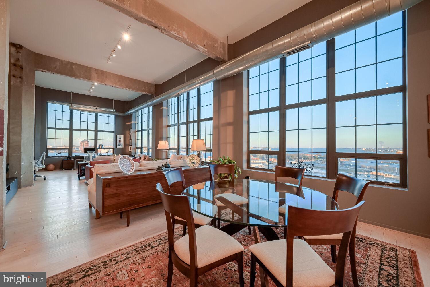 This stunning, architecturally significant corner residence on the 15th floor of Silo Point Tower offers sweeping panoramic water and city views from rare triple exposures to the east, west, and south capturing both breathtaking sunrises and glowing sunsets while illuminating the home with natural light throughout. Boasting over 2,200 square feet, this two-bedroom, two-and-a-half-bath condominium is defined by soaring 14-foot ceilings, dramatic floor-to-ceiling windows, and striking industrial-chic details including exposed columns and ductwork. The light-filled open layout is enhanced by hardwood floors throughout and Lutron motorized blinds. The expansive living and dining areas are perfectly suited for both everyday living and entertaining, seamlessly connecting to a chef’s kitchen featuring a granite center island, tile backsplash, and custom cherry cabinetry with distinctive aluminum band detailing. The luminous primary suite is a private retreat with floor-to-ceiling windows, custom closets, and a spa-like bath complete with a double vanity and oversized glass-enclosed walk-in shower. A well-appointed secondary bedroom offers an en-suite bath, ideal for guests or a private office. This residence masterfully balances grand scale with intimate comfort. Two premium garage parking spaces and a storage unit convey. Experience the coveted Silo Point lifestyle with full-service amenities including 24-hour attendant, on-site management, a state-of-the-art fitness center with yoga studio and treatment room, boardroom, game room, and the spectacular 19th-floor Sky Lounge. Conveniently located with easy access to I-95 and the water taxi, and set in the heart of Locust Point—one of Baltimores most sought-after waterfront neighborhoods offering walkability to parks, dining, and vibrant city living.