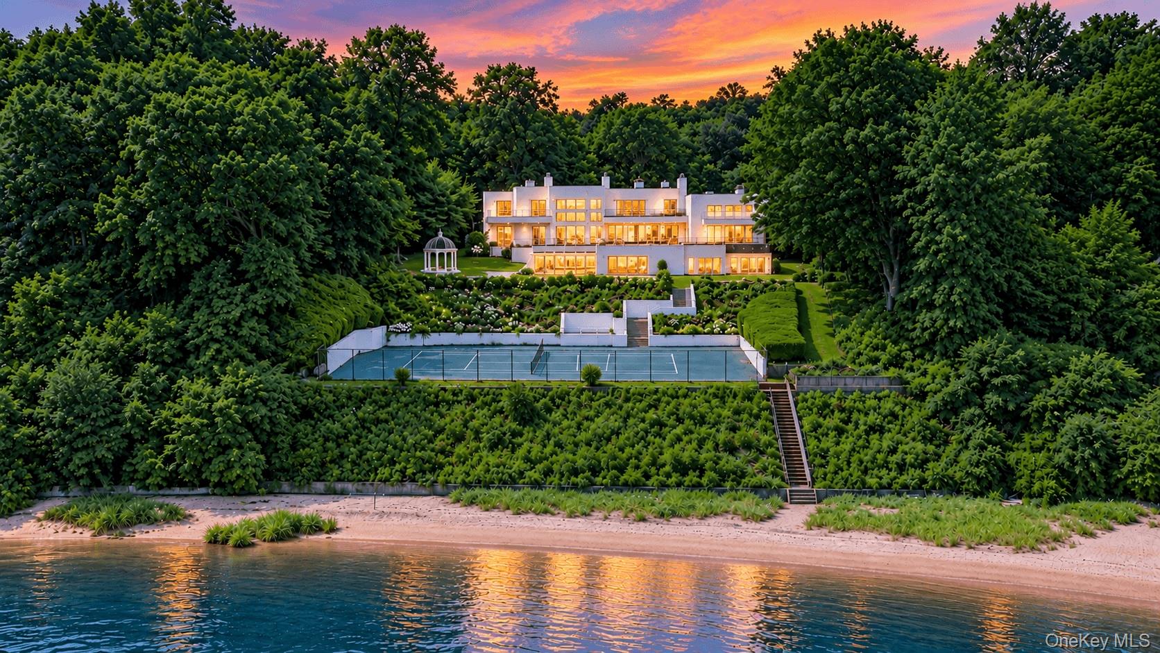 Thalassa Bay is an extraordinary 9,900sf beachfront estate set upon 200ft of direct shoreline on the tranquil waters of Oyster Bay Harbor. This magnificent waterfront sanctuary offers an exceptional luxury lifestyle defined by water, light, privacy, and endless horizons, with an indoor swimming pool and spa, private one-bedroom guest apartment with separate entrance, 4-car garage, tennis court, six fireplaces, billiards room with wet bar, recreation room, expansive gardens, gazebo, and direct saltwater access for swimming, kayaking, boating, jet skiing, and water skiing. Invite family and guests to collect oysters and mussels along the shoreline before gathering for an unforgettable evening dinner, surrounded by walls of glass overlooking the pristine harbor. Thalassa Bay is a private retreat where sophisticated architecture and nature exist in extraordinary harmony. Expansive gardens, gracefully flow toward the water, while each sunrise transforms the harbor into a shimmering palette of gold and rose. A formal driveway framed by stone and granite accents, grand tiered fountain, mature landscaping, and seasonal flowers creates a memorable arrival at the elegant double-door entrance. Upon entering, dramatic water views and soaring spaces immediately establish the home’s remarkable character. Walls of glass, marble floors with brass inlay, designer baths, gourmet eat-in-kitchen, custom railings, architectural details, and beautifully crafted built-ins create an atmosphere of refined elegance. The spectacular Gala Hall features soaring ceilings, panoramic water views, an impressive hand-carved marble fireplace, and an extraordinary backlit and underlit Onyx bar. A Juliet balcony overlooks the fountains and gardens, creating an idyllic setting for morning coffee and quiet reflection.A floating marble staircase and dramatic second-story living room further enhance the architectural presence, while the ever-changing harbor remains a central element of the interior experience. A distinctive European influence flows throughout the residence, with marble, glass, stone, light, and water creating a sophisticated continuity from room to room. The second floor encompasses the sumptuous primary suite, complete with its own fireplace, along with two additional bedroom suites, each featuring a private balcony and beautifully appointed designer bath, creating an intimate retreat overlooking the surrounding gardens and shimmering waters. The lower level offers a private resort experience centered around an indoor swimming pool and spa, dedicated changing room and bath, fireplace, billiards room with wet bar, and recreation room. The private one-bedroom guest apartment provides a comfortable and discreet retreat for family and friends. The surrounding waterfront community of Swan Cove offers a full boat launch, floating dock, and oversized parking area, providing exceptional convenience for boating and entertaining. Additional parking accommodates large gatherings, a golf cart may offer a charming way to transport guests between the waterfront and main residence.  Thalassa Bay is a rare North Shore beachfront estate where architecture, landscape, and water converge to create a truly distinctive way of life. Here, the horizon is not simply a view; it becomes part of everyday living. View 3D tour and Floor Plan.