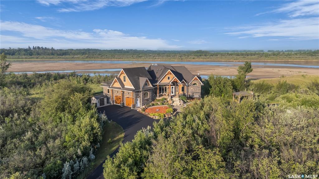 Live the Riverfront Dream. A Truly Exceptional Home. Set on an incredible 32-acre lot with 12 acres of private riverfront, you won’t find another property like this! Offering over 5000 sq ft of living space, the award-winning Durette Acreage makes an unforgettable first impression with its striking roofline and dramatic front elevation. Inside, soaring vaulted ceilings, stone fireplaces, and panoramic river views create a sense and scale with timeless style. While the craftsmanship and natural wood details ground the home bringing a feeling of warmth and intimacy. At the heart of the property is a space designed to bring everyone together: a custom walnut kitchen—seamlessly connecting to the family room and breakfast nook, which opens onto the wraparound balcony (a perfect spot for our Saskatchewan sunsets). The luxurious primary suite is sensational: coved ceilings, river views, spacious walk-in closet, and a spa-inspired ensuite. Upstairs, a private loft suite with full bathroom offering options for bedroom or home office space. Downstairs, the 3 bedroom walkout level with its 9-foot ceilings opens into a large family room and games area, divided by a beautiful gas fireplace. A home theatre room is for the kids and the custom built wine room is perfect for wine lovers or collectors. Step outside into the acreage lifestyle of your dreams. You’ll find a handcrafted gazebo with a wood-burning fireplace. Peaceful corners for morning coffee. A lower patio designed for late-night s’mores and unforgettable family moments. Bold. Luxurious. One-of-a-kind. This isn’t just a house , it’s the place you’ll build a lifetime of priceless memories with your family.