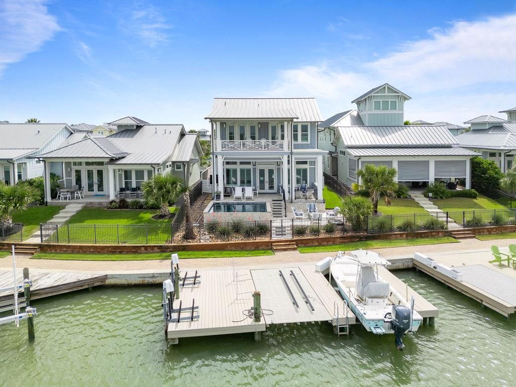 WATERFRONT | POOL | FOUR BEDROOMS | BOAT LIFT | FURNISHED. Welcome to an extraordinary waterfront retreat where luxury and coastal charm blend effortlessly. Perfectly positioned along a premier canal, this beautifully crafted residence offers convenient and fast bay access, timeless design, and a lifestyle tailored for those who appreciate the finer things. Step inside to soaring ceilings, and a sunlit, open-concept layout anchored by a designer kitchen featuring a large island, bar seating, a gas cooktop, and ample cabinetry. Whether entertaining or simply enjoying a quiet morning, every detail has been thoughtfully curated—from the plantation shutters to the soft coastal tones that carry throughout the home. The living and dining spaces flow gracefully to a covered patio, where a sparkling inground pool and inviting fire pit lounge offer the perfect setting for sunset gatherings. A private dock with boat lift and kayak launch awaits just steps away, making spontaneous days on the water feel effortless. Upstairs, the primary suite is a serene sanctuary with its own covered balcony overlooking the canal. The en suite bath features a walk-in shower, dual sinks, and a generous walk-in closet, offering both beauty and function. A versatile bonus space includes a wet bar with wine fridge and sink, ideal for guest overflow or a cozy second living area.  Thoughtful extras include an automatic storm shutter system, utility room with sink and built-in cabinetry, a detached garage, and a quaint fenced yard perfectly suited for four-legged companions. Every corner of this home reflects coastal sophistication and livability. With a perfect balance of elegance and ease, this is where everyday moments become unforgettable. The garage is long enough to accommodate a boat! Don't miss the out door grilling and chilling area with grill, sink and fridge. PLUS a work shop in garage!