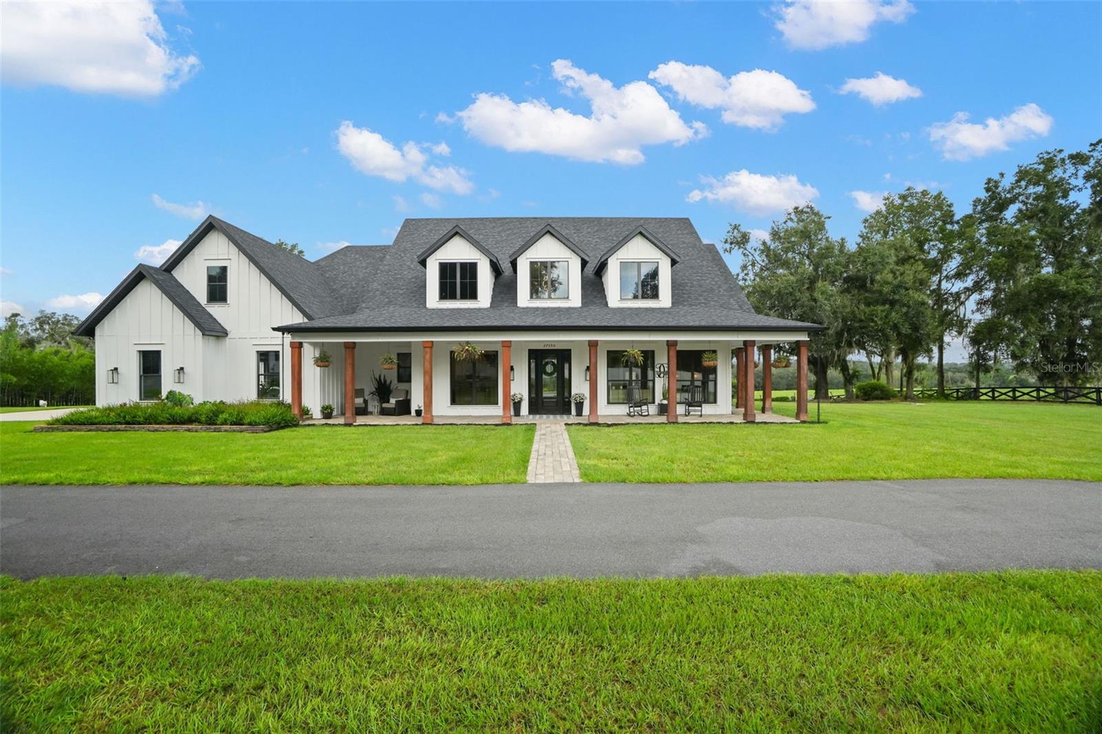 Perched on over three acres of elevated, private grounds framed by majestic grandfather oaks, this gated custom estate offers an exceptional blend of exclusivity, luxury, and resort-style Florida living. With over 20ft of elevation change across the property, the setting enjoys a rare sense of prominence, openness, and privacy. The estate unfolds as a secluded retreat. A paved drive leads to the residence and detached barn, while an expansive wraparound porch captures the tranquil surroundings and hilltop views. Step inside the grand foyer and your eye is drawn through the home to the resort-style outdoor living area beyond. Disappearing pocket sliders create a seamless connection between the interior and the 30-by-19-foot heated saltwater pool and spa. Inside, wood-look plank tile flows throughout the main living areas. A private den with custom built-ins provides a dedicated home office, while the spacious living room is anchored by a striking stone fireplace. At the heart of the home, the chef’s kitchen features leathered quartz countertops, custom 42" soft-close cabinetry extending to the ceiling with glass-front uppers, a butler’s pantry, pot filler, oversized 68" Electrolux refrigerator and freezer, Bosch dishwasher, built-in oven and microwave, and a large center island with beverage refrigerator. The split-bedroom floor plan provides privacy for owners and guests. Spacious secondary bedrooms share a Jack-and-Jill bath, while the primary suite serves as a private retreat with elegant coffered ceilings and a spa-inspired ensuite featuring dual vanities, marble countertops, and an oversized walk-in shower. A full-size window within the shower overlooks the secluded garden. The ensuite flows directly into an expansive custom walk-in closet with a center island chest of drawers, connecting to the laundry room. The laundry room is fully equipped and includes a custom-tiled pet shower. Upstairs, a private theater creates the ultimate entertainment space, complete with stadium seating, a large screen, and kitchenette with beverage fridge perfect for movie nights, sporting events. Outside, the elevated setting and acreage create a private resort feel. The pool area features a sun shelf and expansive deck, low-maintenance turf, ambient string lighting, and three dramatic fire bowls. A high-top table with a center fire pit provides another gathering space overlooking the pool, while a concrete walkway leads to a secondary fire-pit and lounge area. Built-in speakers inside and out provide the perfect backdrop for entertaining or enjoying the property. Adding versatility is a detached three-part barn offering approximately 900 square feet divided into three distinct spaces. One section is a finished, climate-controlled flex space with a kitchenette, full bath, and mini-split A/C; another is configured as a private gym with wall-to-wall mirrors; and the center bay provides ample storage for lawn equipment, recreational gear, and more. Additional features include an oversized three-car garage, a private archery range at the far end of the property, landscaped grounds, ample parking, and a leased 500-gal propane tank. From its commanding hilltop setting and over three private acres to the resort-style pool and spa, dedicated theater, detached barn, and thoughtfully designed custom interior, this estate offers something increasingly difficult to find in Florida: space, elevation, privacy, and luxury—all in one exceptional property.