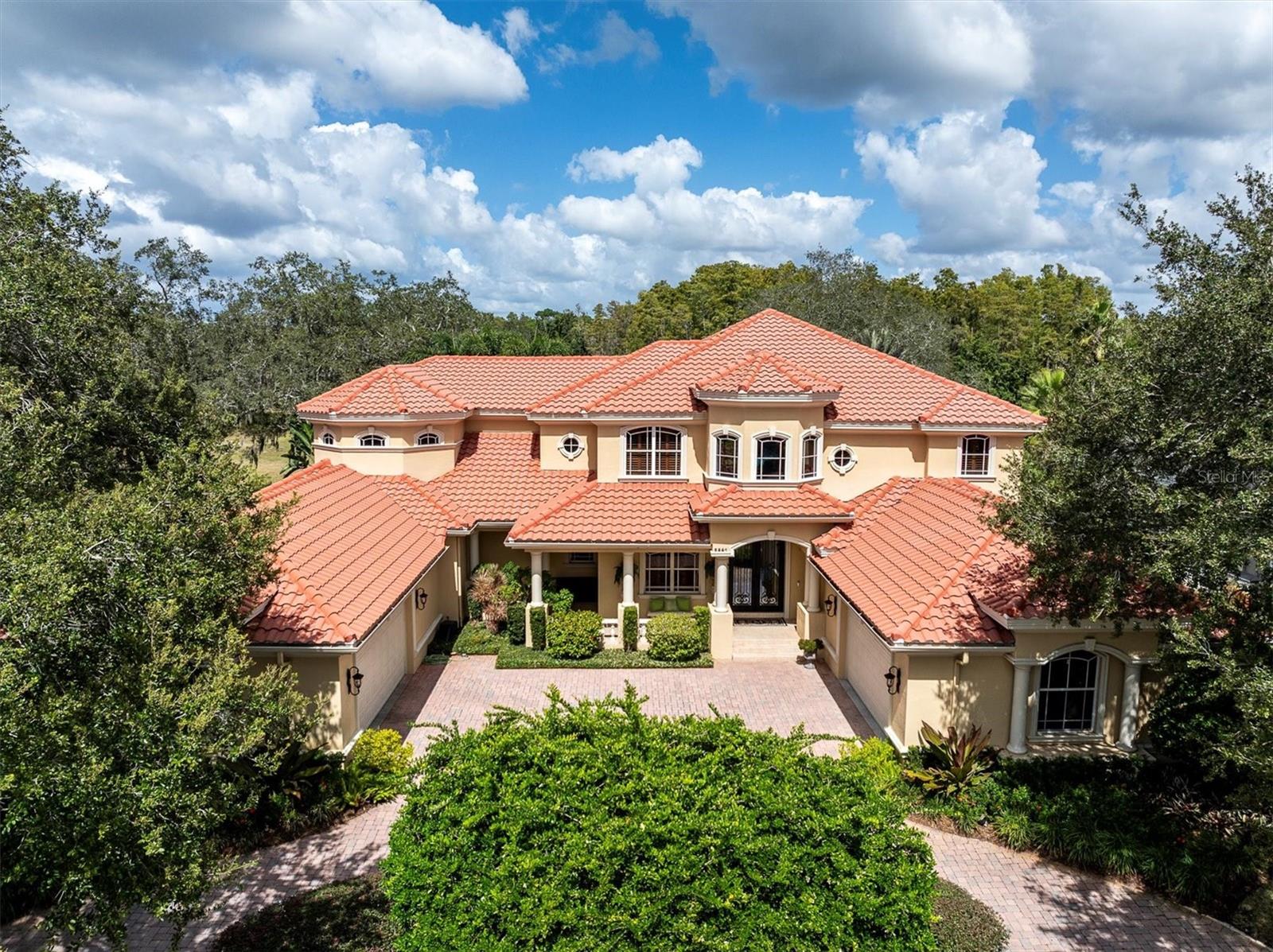 Welcome to this exquisite custom-built estate home perfectly situated in the prestigious guard-gated community of Wentworth. Nestled on a quiet cul-de-sac and overlooking hole #8. This two-story Mediterranean masterpiece offers the perfect blend of luxury, comfort, and thoughtful design. Boasting nearly 5,800 sq. ft. of exceptional living space, this home has been meticulously maintained and upgraded with the finest finishes and details throughout. The spacious gourmet kitchen is a chef’s dream, featuring custom cabinetry, granite countertops, a large island, butler’s pantry, breakfast nook, pot filler faucet, and top-of-the-line appliances. The first floor also includes a grand living area with surround sound, formal and casual dining spaces, a billiard room, a dedicated exercise room with equipment that conveys, and a beautifully appointed home theater featuring a 122” screen—equipment and furniture convey. Upstairs, the luxurious master suite offers a private retreat with a sitting area, two custom-built walk-in closets, and a private balcony overlooking the golf course. The spa-like master bath showcases elegant finishes, creating a serene and relaxing atmosphere. Designed for both entertaining and everyday living, this home features two laundry rooms (one on each floor, with the downstairs updated in 2023), tankless water heater and one traditional water heater, central vacuum system, travertine and wood flooring throughout. The 4-car garage with golf cart garage includes epoxy floors, offering both beauty and function. Step outside to your private resort-style oasis with an extended covered veranda, custom lagoon-style pool, and spa with PebbleTec Ocean Blue finish, three waterfalls, and marble-accented Lightstreams tile (pool renovated 2022–2023, $230k). The outdoor kitchen makes this an entertainer’s paradise, all within a fenced backyard surrounded by tropical landscaping. Additional updates and features include three new A/C units with 10-year warranty (2023), new front door (2024), outdoor lighting (2023), whole-house generator, updated home theater system (2023), ADT security system with cameras covering the entire property, a reverse osmosis system (2024), and a 100-bottle wine cooler. Conveniently located in the East Lake corridor near top-rated schools, beaches, and shopping, this stunning estate truly has it all—luxury, function, and timeless appeal in one of Pinellas County’s most sought-after communities. Must see to apppreciate!