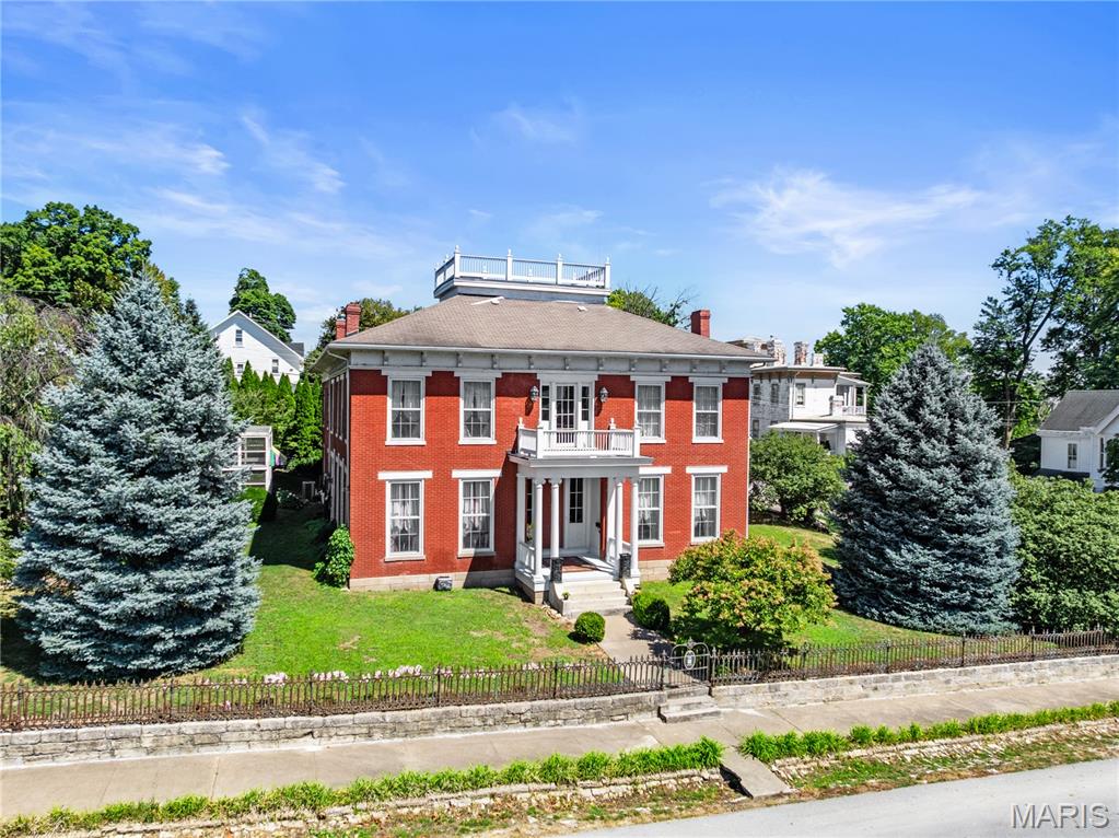 Known as the Edward G. McQuie Home, this historic residence in Louisiana, Missouri, blends rich heritage with versatile living. Built in 1857 during the town’s first period of affluence, the brick home and wrought iron fence showcase timeless architecture. From the rooftop widow’s walk, you can enjoy views of the Mighty Mississippi and Illinois beyond. The main floor features formal living areas, including a living room, parlor, and dining room, while the kitchen boasts abundant cabinetry, a SubZero refrigerator, and Gaggenau appliances. The second floor features four bedrooms, including a spacious primary suite with dual sinks, a soaking tub, and a separate shower with multiple body sprays. An adjoining bedroom serves as a sitting room. Two additional bedrooms share a hall bath, while a fourth enjoys its own en-suite bath. A conveniently located second-floor laundry adds modern functionality. The renovated third-floor attic provides a stylish bonus living space. Enhancing the property is a three-car carriage house with guest quarters and a full bath, plus a charming greenhouse and landscaped grounds. Steeped in history yet designed for today, the Edward G. McQuie Home presents a rare opportunity to own a landmark piece of Missouri heritage.