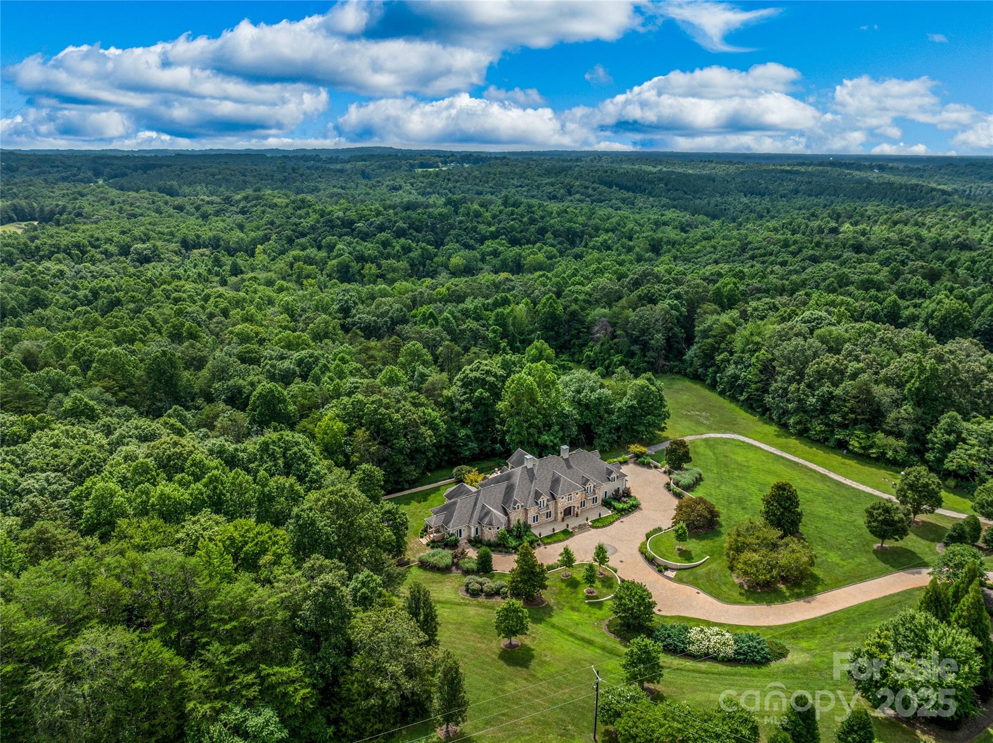 Experience unparalleled luxury, quality craftsmanship, and abundant spaces at this one-of-a-kind property! A stunning brick paver driveway framed by meticulous landscaping welcomes you home. The main level is perfect for entertaining, showcasing a great room with custom library, family room, dining area, and chef’s kitchen with plentiful storage. Ascend via the grand curved staircase or elevator to the upper level, home to the primary suite and additional bedrooms. The primary suite features a private covered balcony, while the opulent bath boasts a steam shower, soaking tub, walk-in closet, wet bar and laundry area. The lower level offers additional finished spaces, including a kitchen, living area, bonus rooms, and full bath. The +-27 acre property offers complete privacy, open spaces, and potential areas to create pastures. All considered, this home offers an exceptional value that is rarely found, perfectly blending top tier construction quality and charm with a spacious floorplan.