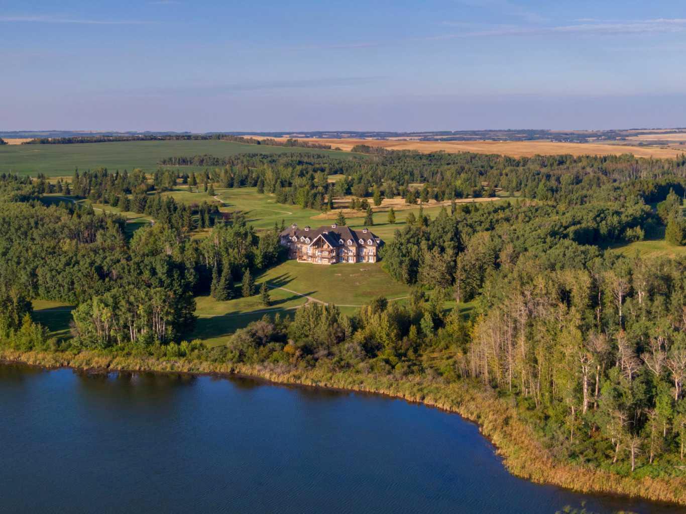 Located in the quiet, picturesque countryside of Lacombe County, the Gadsby Lake Estate is a once in a lifetime opportunity to own a secluded paradise offering just about everything you can dream of. Opulent architectural features and exquisite design elements are found throughout both the main residence and adjacent lodge, including the use of one-of-kind building materials from around the world. In addition to the 17 bedrooms and 31 bathrooms, this stunning estate boasts several specialty rooms including a library, a bright and airy atrium, a sauna and gym, large wine cellar, an indoor pool and lounge, a grand party room, private theatre, and games room. Each space is impeccably designed with elegance, comfort, and convenience in mind. Beautiful windows and outdoor seating lounges, deliver both spectacular lakefront views, and a feeling of tranquility and connection to the serene natural surroundings. Gorgeous stone fireplaces, rich wood accents, and suite-style guest quarters with spa-like ensuites create a warm, welcoming environment for owners and guests alike. A multitude of recreational amenities just for you can be found throughout the Estate’s almost 300 acres. Hiking, fishing, canoeing, and  tennis courts are just some of the activities that can be enjoyed in the utmost privacy., whenever you’d like. The property also features paved and natural pathways through seemingly endless secluded parkland. Rolling hills, elaborate landscaping and lush gardens create an oasis unlike any other you’ll find in Canada.