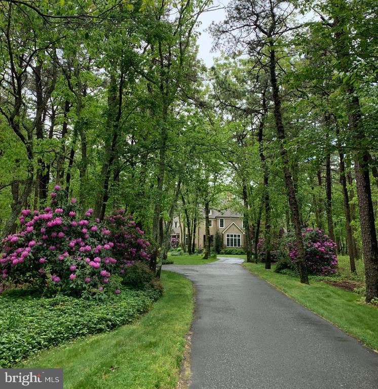 Nestled within the exclusive Preserve at Little Mill community, this extraordinary luxury residence offers a rare blend of privacy, elegance, and timeless character, set against the backdrop of a picturesque golf course. Tucked away on a secluded lot with a circular driveway, three-car garage, and breathtaking natural landscaping, this home feels like a private retreat from the moment you arrive. Thoughtfully included spring and summer photos showcase the lush gardens curated by a passionate gardener, helping buyers envision the property in full bloom beyond the winter season.The exterior’s modern French Provincial aesthetic, with stucco finishes and climbing vegetation, sets the tone for what awaits inside. A charming porch overlooks the golf course, offering serene views in a peaceful, private setting. Step into the freshly painted, elegant foyer where new 4” oak floors create a dramatic and welcoming first impression.The living room is truly breathtaking—anchored by a newly renovated engineered limestone fireplace, soaring two-story cathedral ceilings, custom built-ins, and a stunning modern chandelier. A wall of windows floods the space with natural light and opens directly to a spacious patio, perfect for indoor-outdoor entertaining.The chef’s kitchen is a statement in both function and design, featuring an oversized quartzite island, granite countertops, quartzite backsplash, and an exceptional appliance package including a Lacanche 5-burner double-oven range, Sub-Zero refrigerator, Vent-A-Hood, ZLINE microwave drawer, JennAir dishwasher, and farmhouse-style butler sink. Custom cabinetry abounds, while barn doors leading to the walk-in pantry and a rustic wood beam above the breakfast nook add warmth and authenticity—beautifully preserving the home’s French Provincial charm.The main level also offers a versatile TV room with pocket doors, ideal for entertaining, and an elegant executive office accessed through French doors. The primary suite, privately located on the main level, is a true sanctuary. Behind French doors, enjoy two walk-in closets and a spa-like en suite bath featuring a soaking jacuzzi tub perfectly positioned to overlook the tranquil natural surroundings.An evocative, designer powder room adds yet another layer of character and sophistication.Upstairs, you’ll find four generously sized bedrooms, a study area, and three additional full bathrooms, offering flexibility for family and guests alike.The newly finished basement (completed this summer) provides a bright, modern canvas for the next owner. Luxury vinyl plank flooring, fresh paint, a full bathroom, and expansive unfinished space make it ideal for recreation, a home gym, workshop, or additional storage.This home is truly one of a kind—rich in character, thoughtfully designed, and impossible to replicate. More than a house, it’s a retreat away from the hustle and bustle, yet conveniently located across from the golf club on Hopewell Road, where exceptional dining awaits.Don’t miss this rare opportunity to call this remarkable property your own.