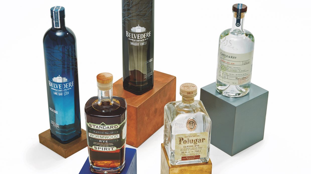 Bottles of various rye spirits that aren't whiskey rest upon different colored platforms against a white background.