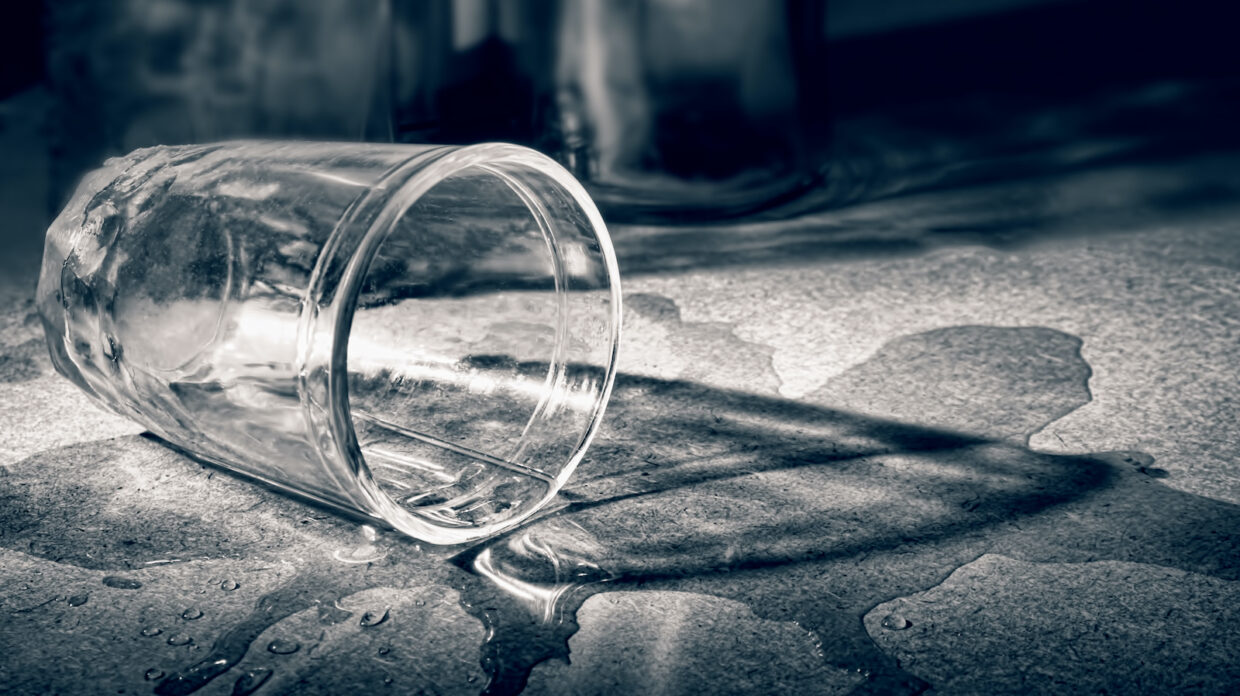 a spilled glass of whisky on a table in black and white