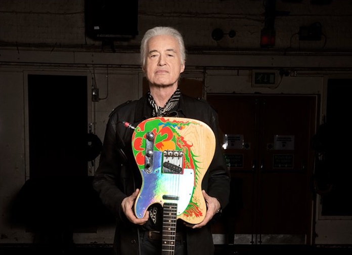 Jimmy Page com os cabelos grisalhos pesos para trás, pousando com sua guitarra colorida, em tons de azul, verde, vermelho e madeira, de ponta cabeça. Ele está de blusa preta.