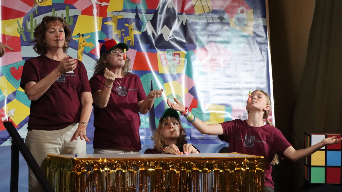 Our brave contestants are balancing dice on crafts sticks in their mouths.